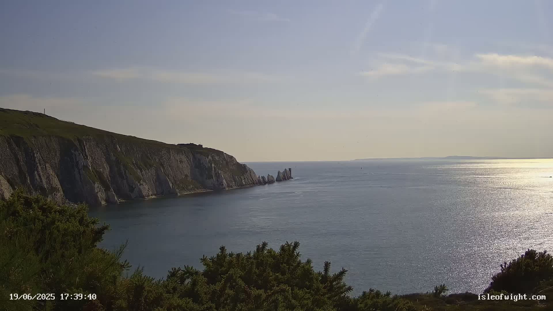 White cliffs meet a calm, sunlit sea under a mostly clear sky.