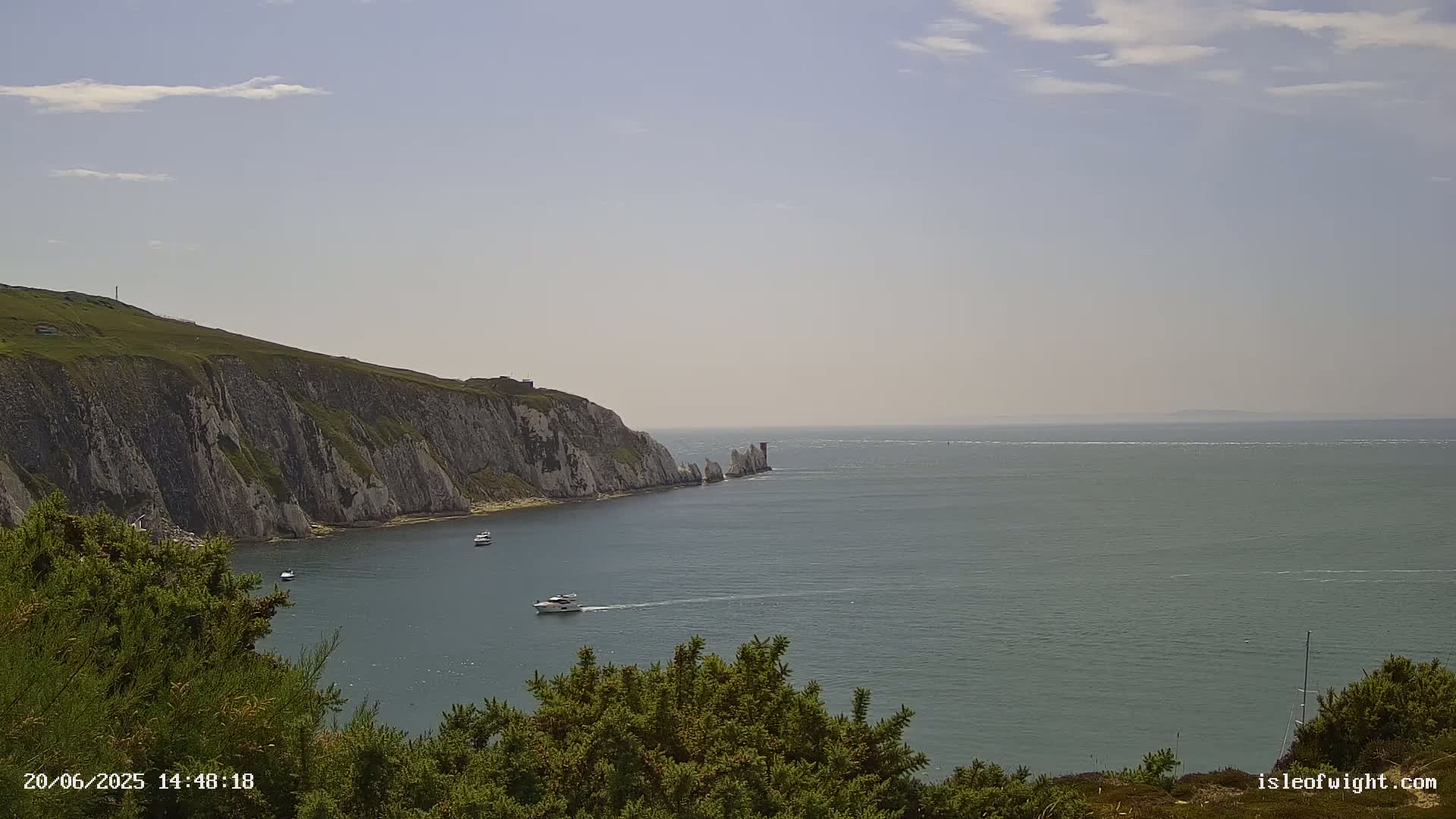 A partly cloudy day reveals a scenic coastal view of white cliffs, a lighthouse, and several boats on calm waters.