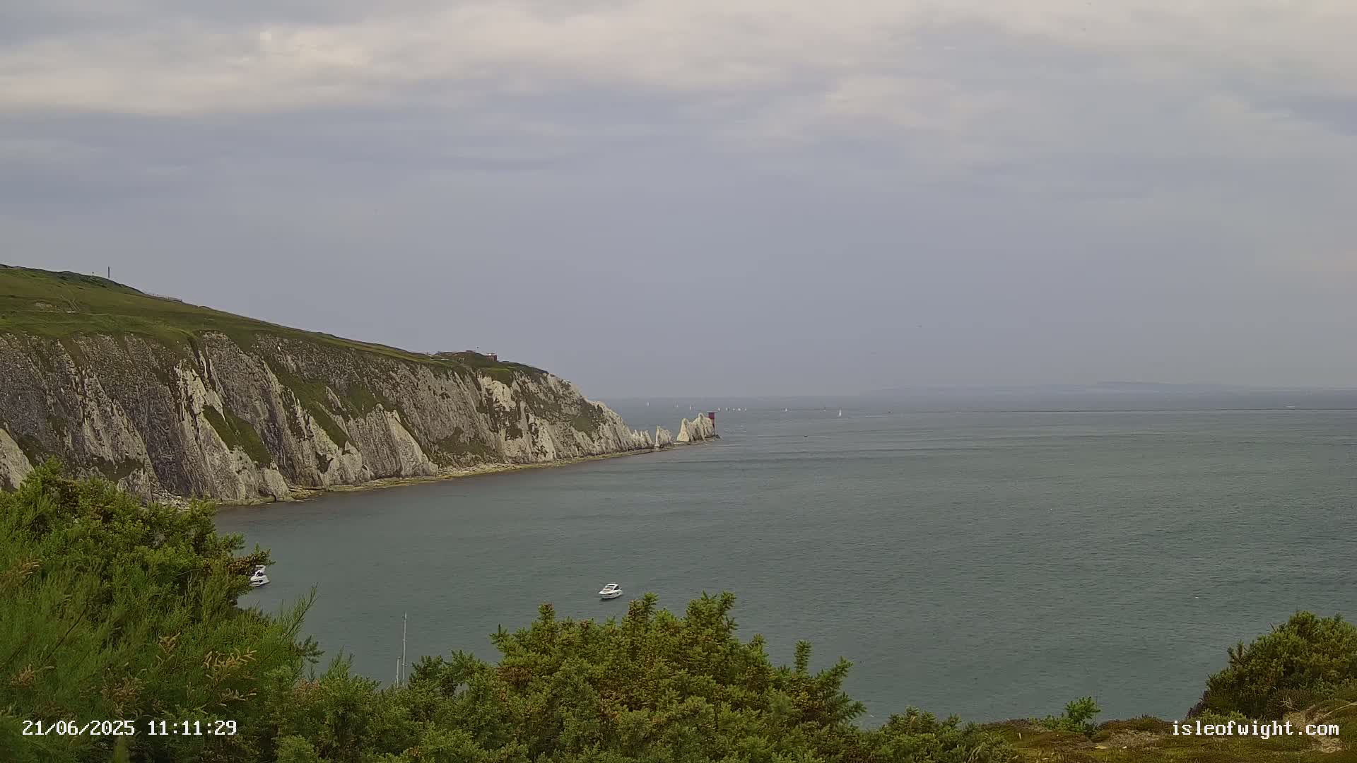 White cliffs and several small boats are visible on a calm, overcast day, overlooking a large body of water.