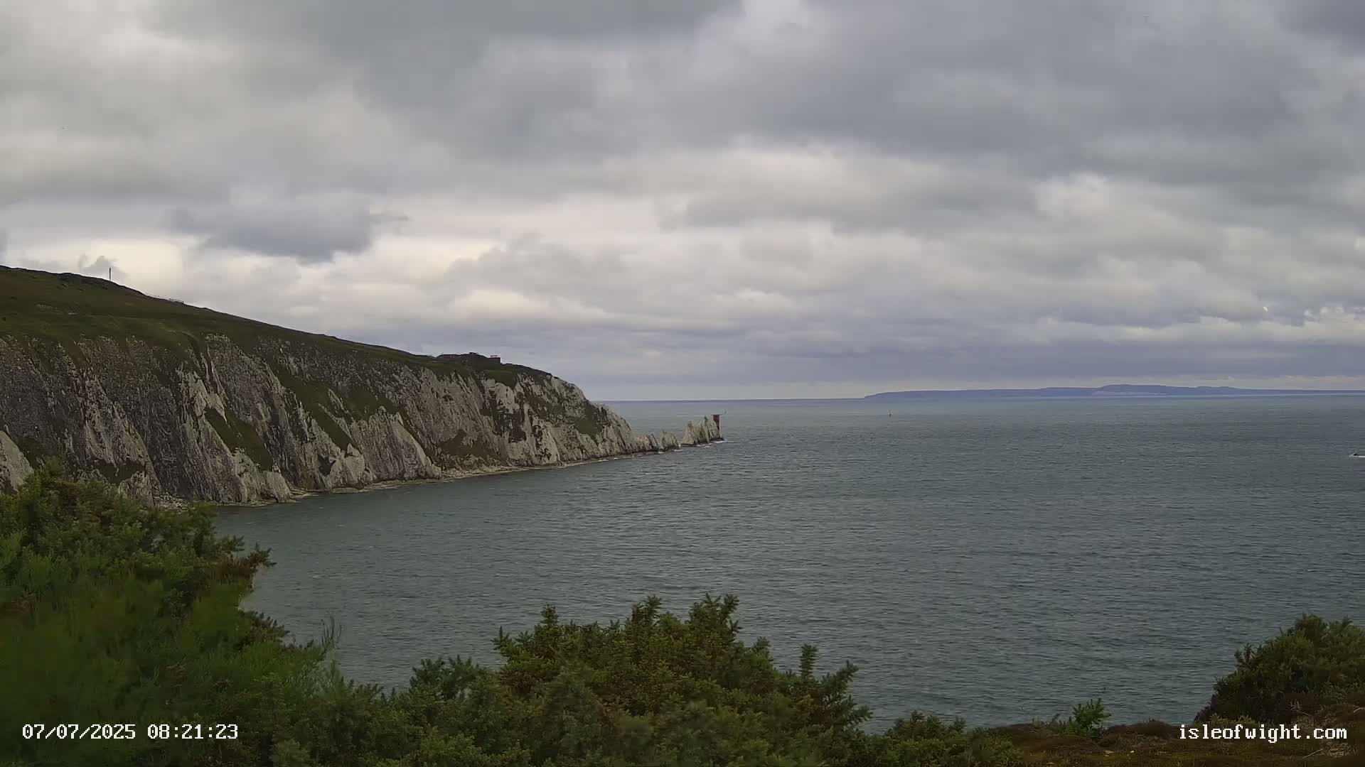 A coastal scene shows a rocky cliffside and a calm, gray sea under an overcast sky.