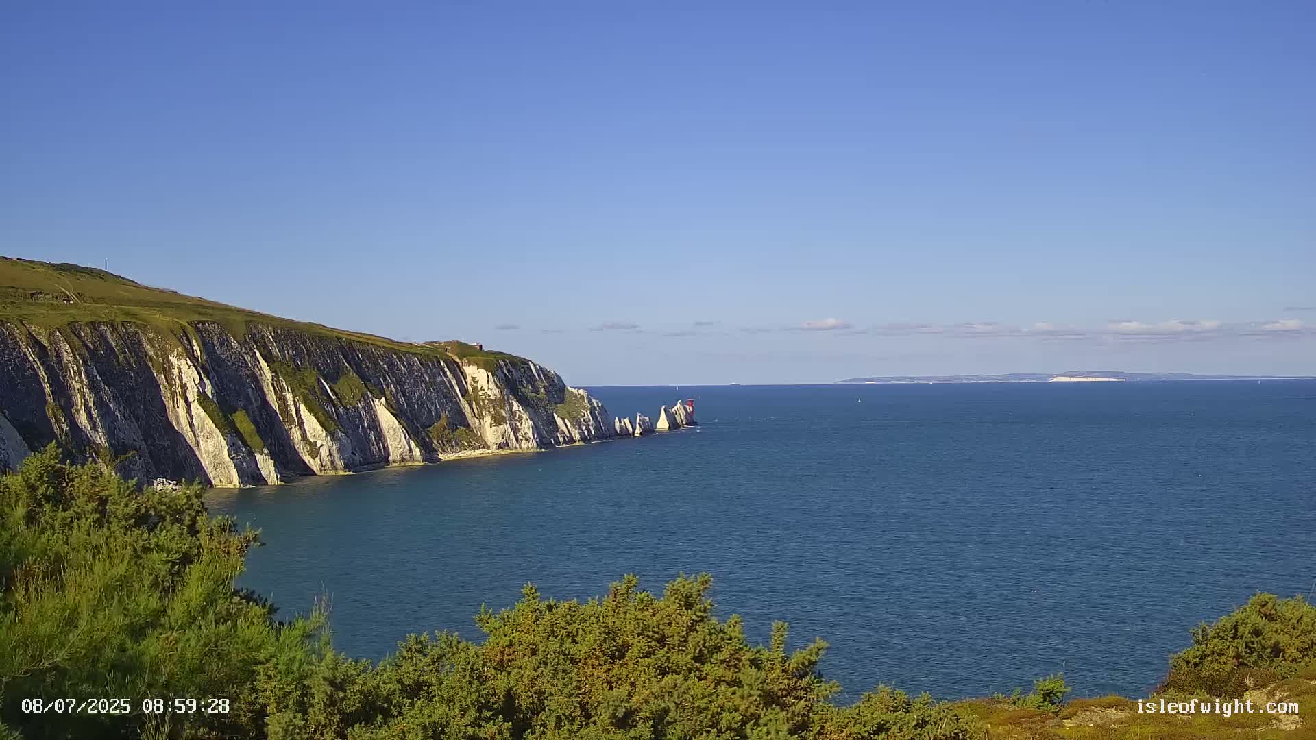 White cliffs and a body of water extend to a distant landmass under a clear blue sky.