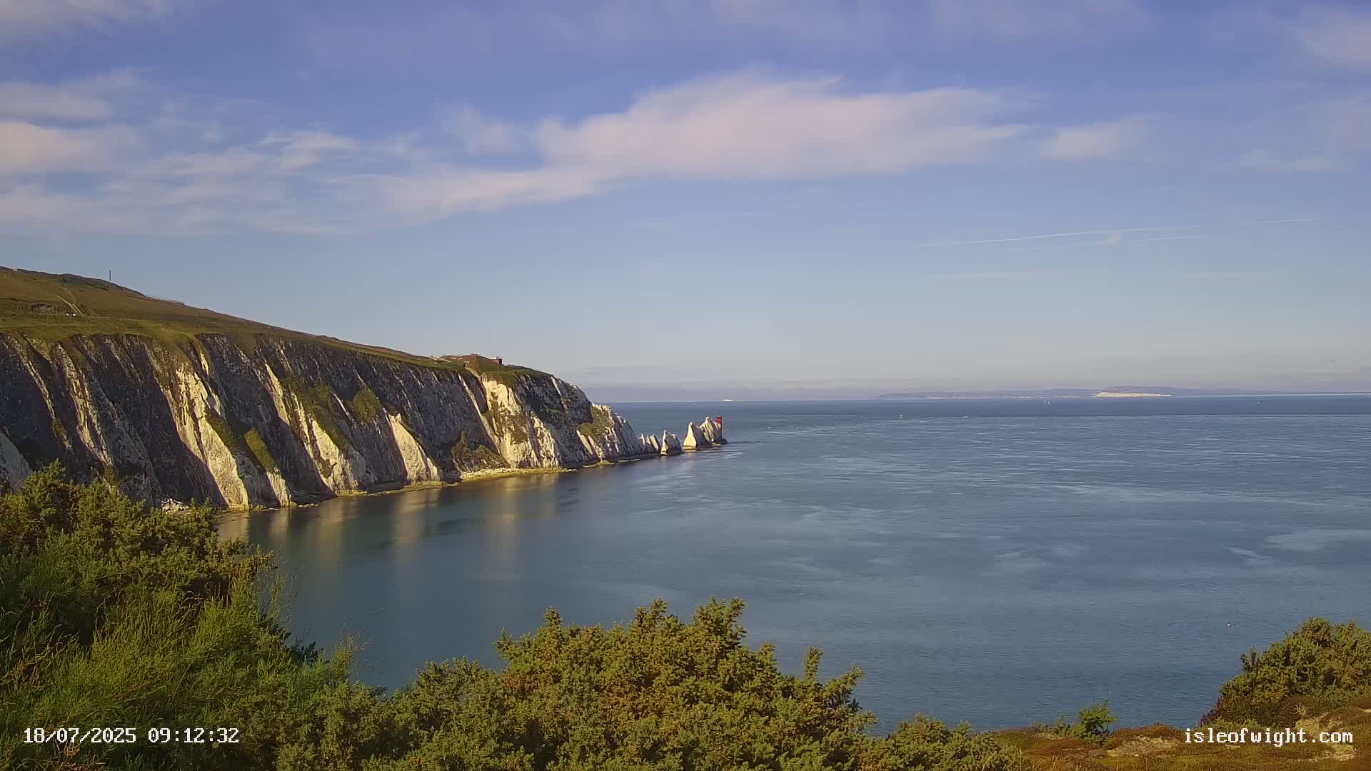 White cliffs and stacks rise from a calm sea under a mostly clear, sunny sky.