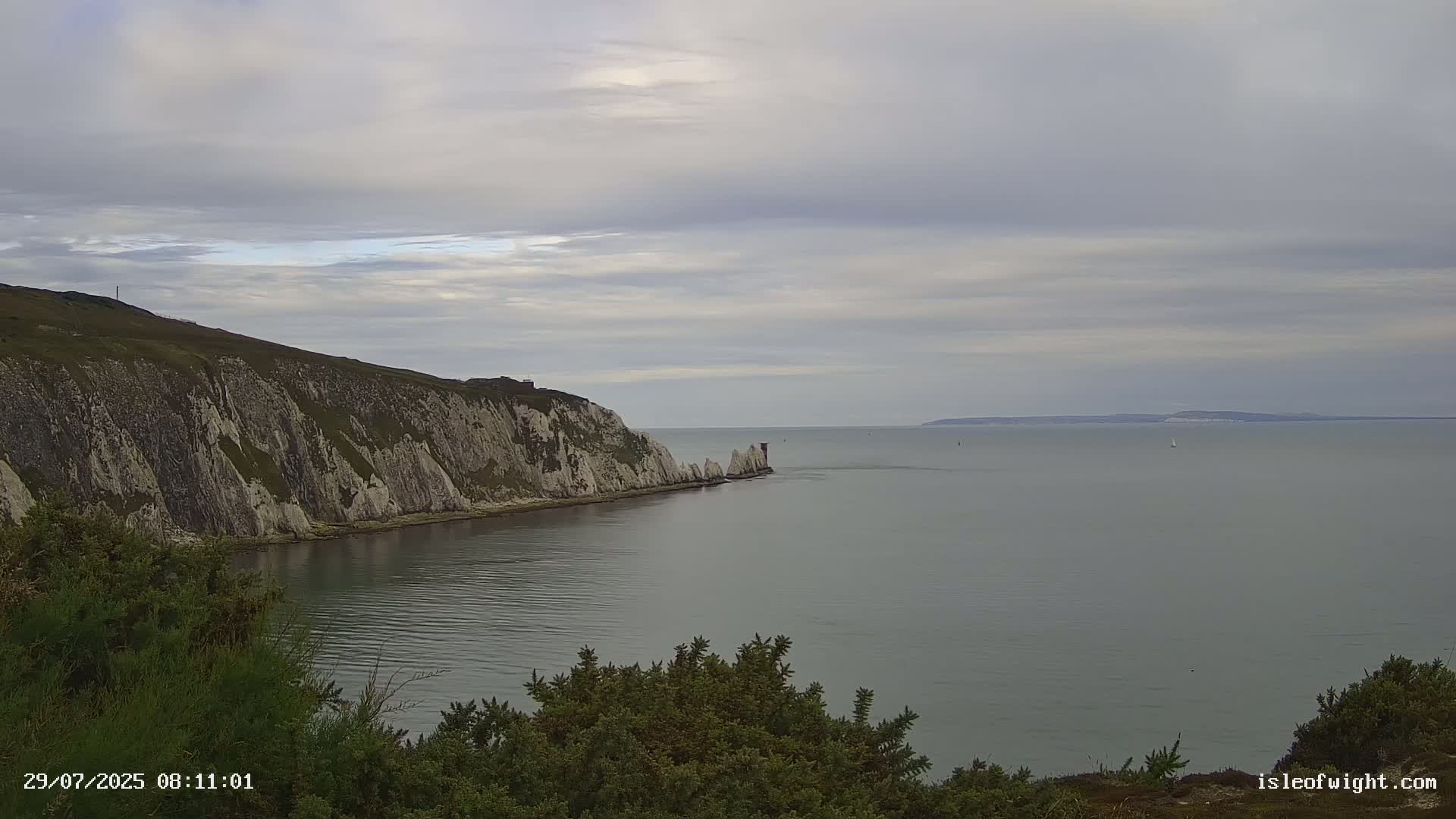 White cliffs meet a calm, grey sea under a cloudy sky.
