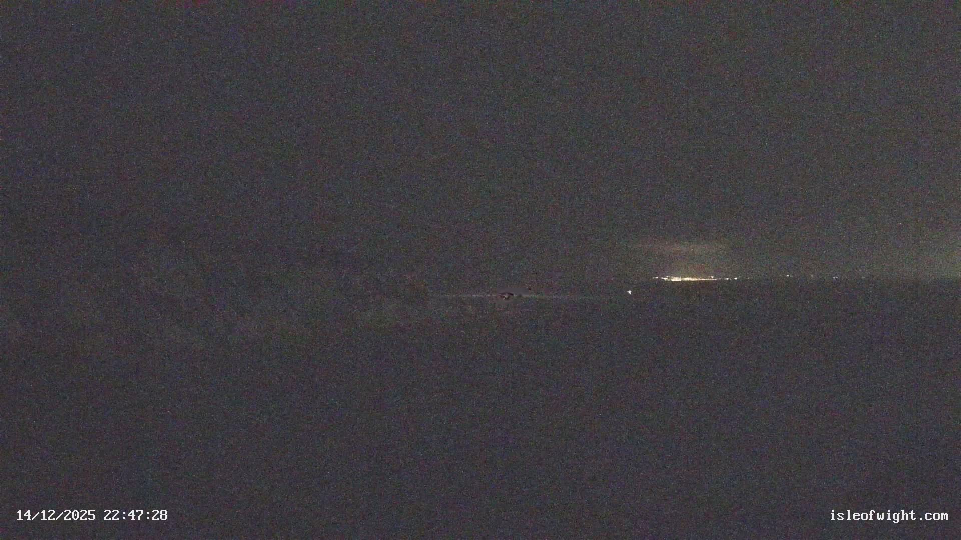A coastal landscape on a mostly cloudy morning features prominent white chalk cliffs and The Needles lighthouse reaching into the choppy sea, with distant land glowing faintly on the horizon.