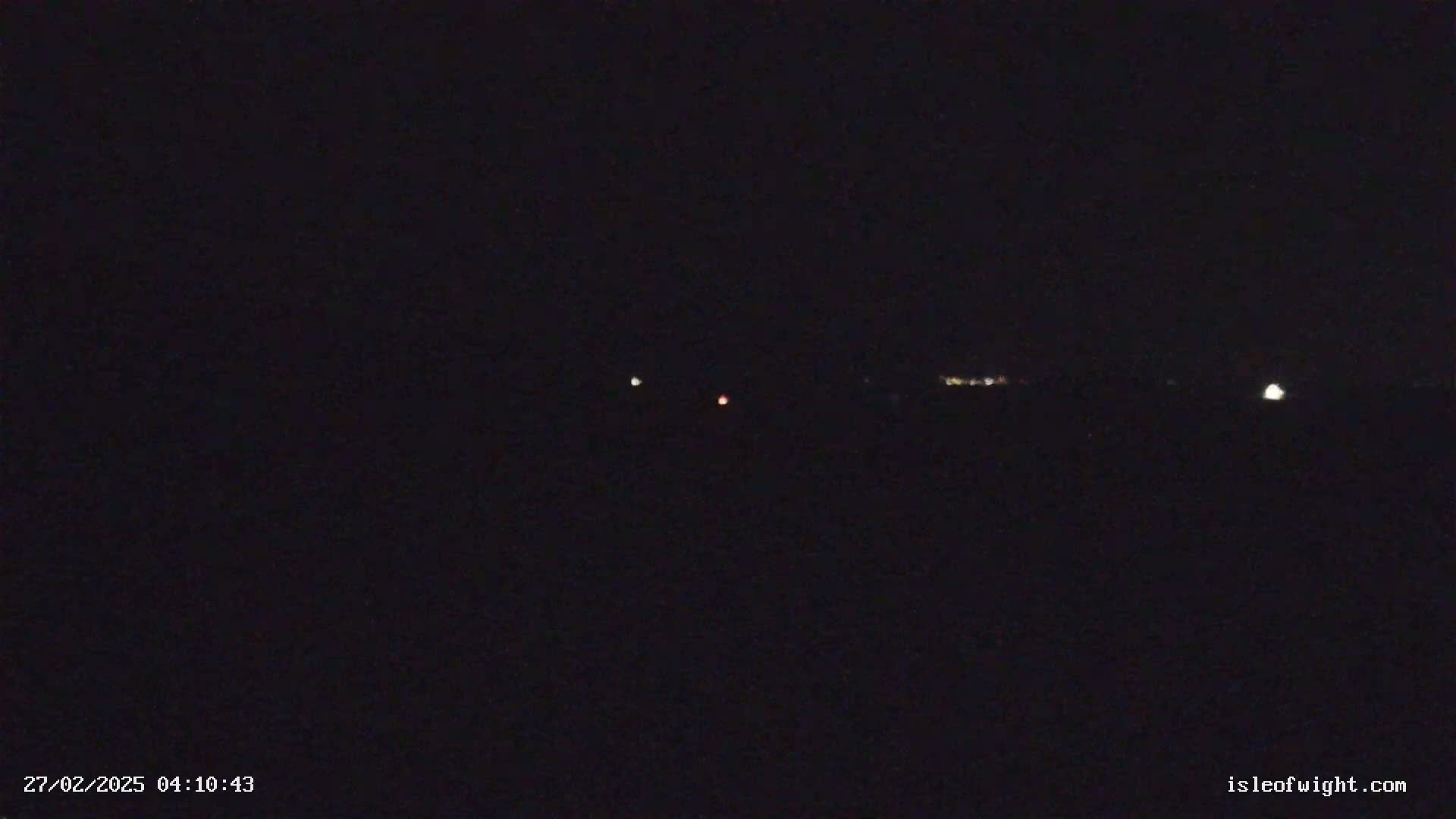 A nighttime, dark image shows a few distant lights on the horizon.