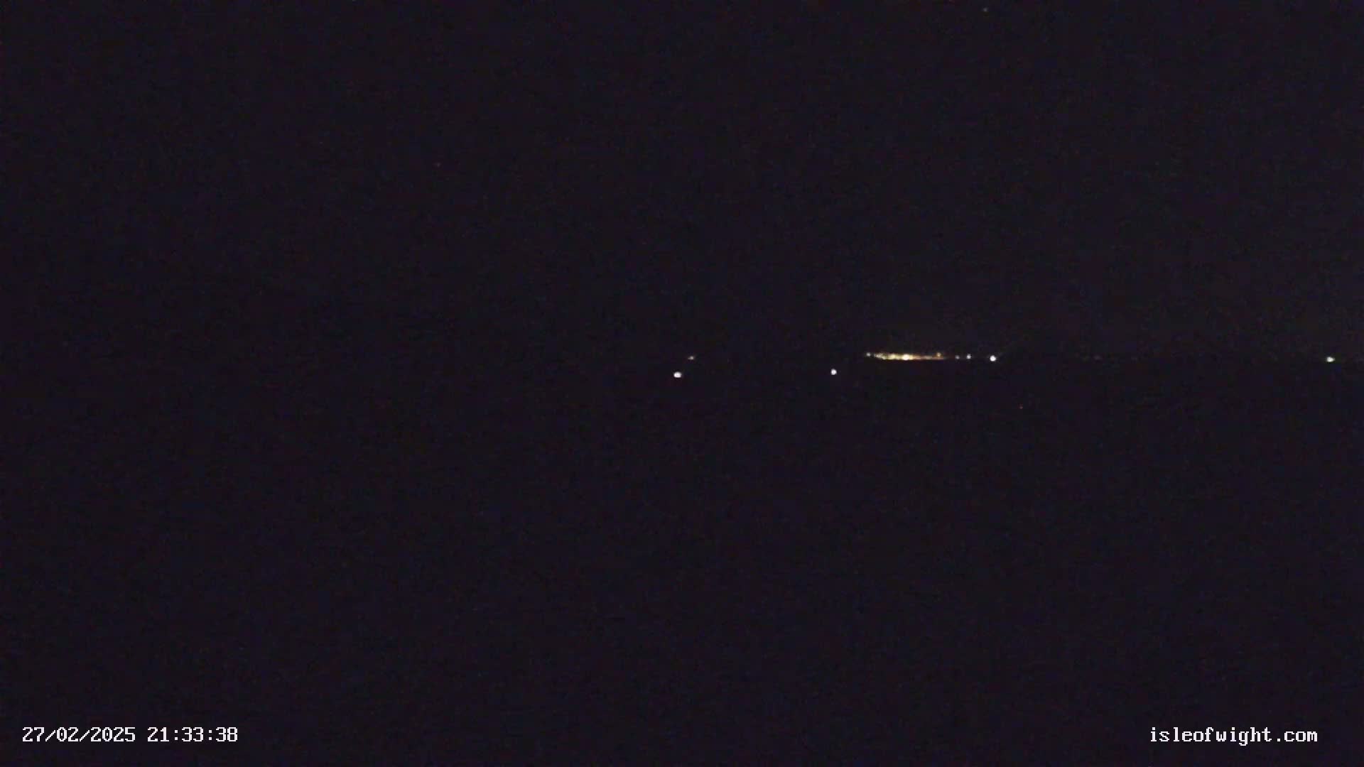 A dark, nighttime scene shows a faint, distant line of lights on the horizon under a clear, starless sky.