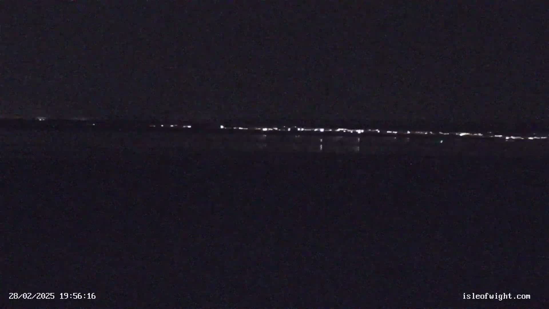 A nighttime, long-distance view of a line of lights across a dark body of water under a clear sky.