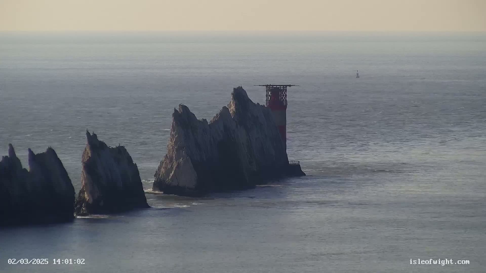 A lighthouse stands atop a rocky outcrop in the sea on a hazy day.