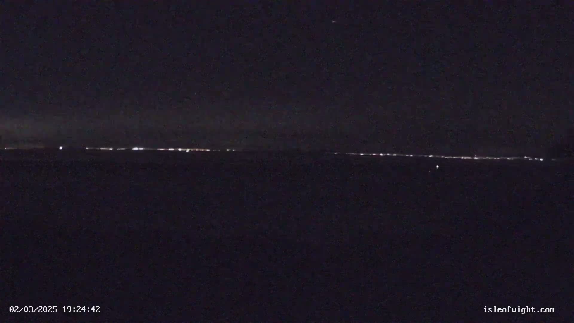 A nighttime long shot shows a distant line of city lights on the horizon under a clear, dark sky.