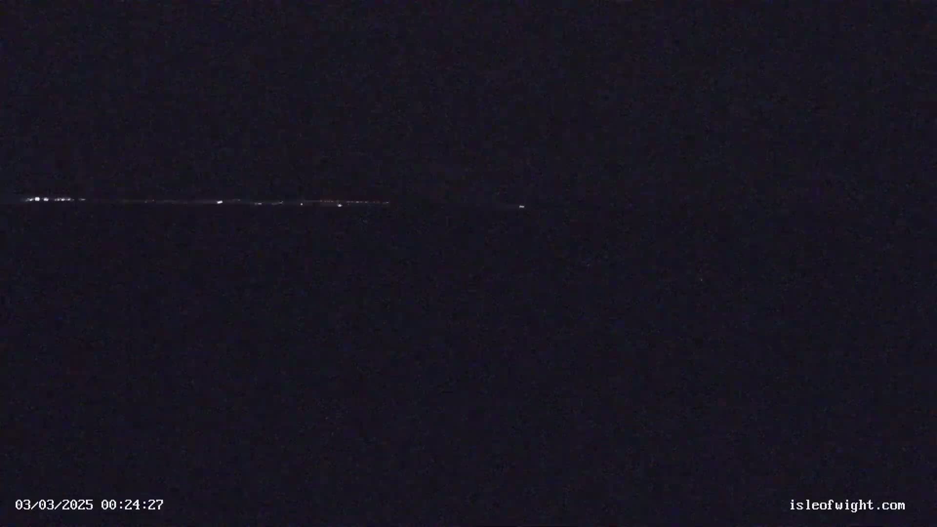 A low-light, nighttime image shows a distant line of faint lights on the horizon.