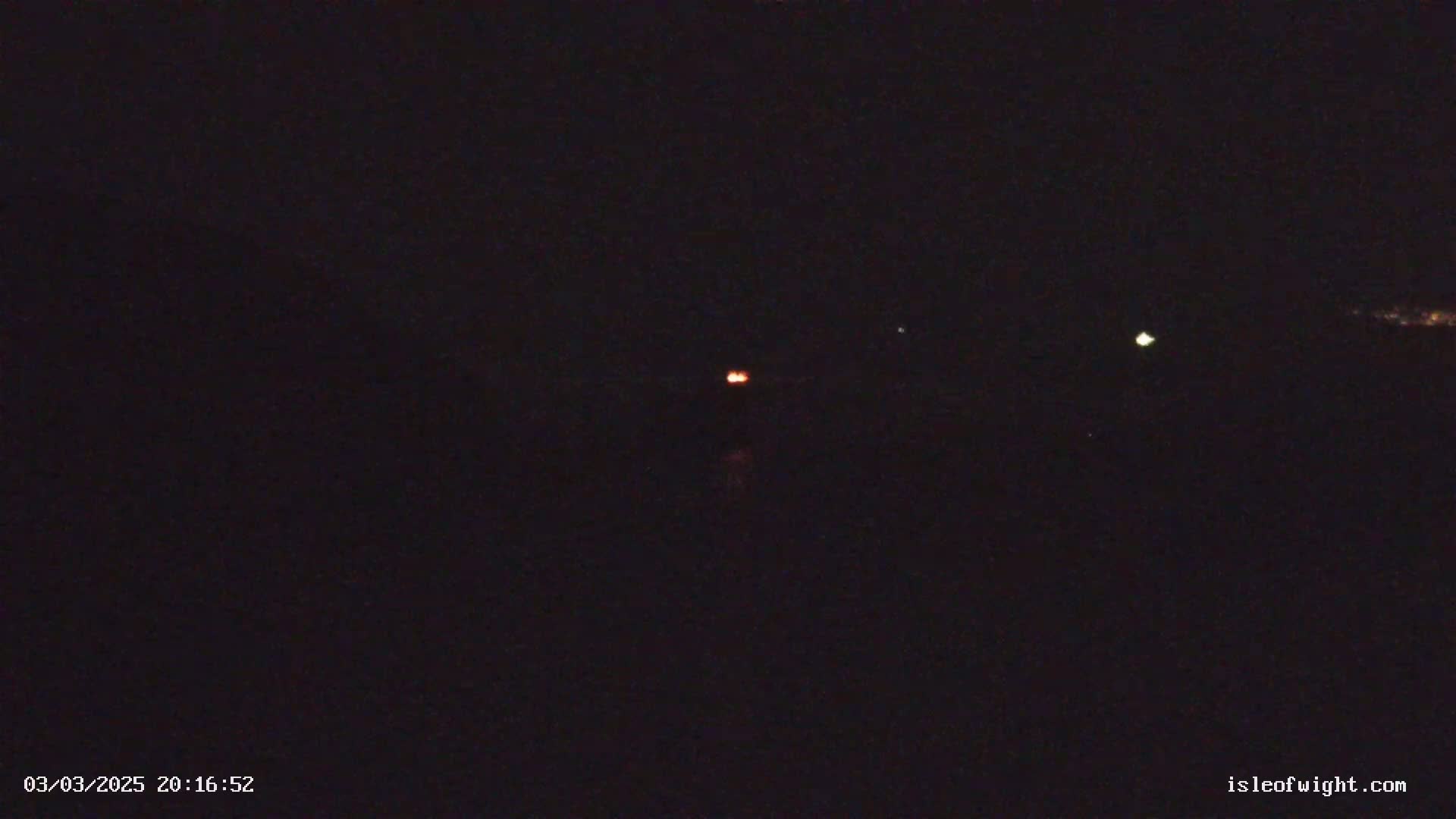 A dark, nighttime scene shows three small, distant lights; one orange, one green, and one white.