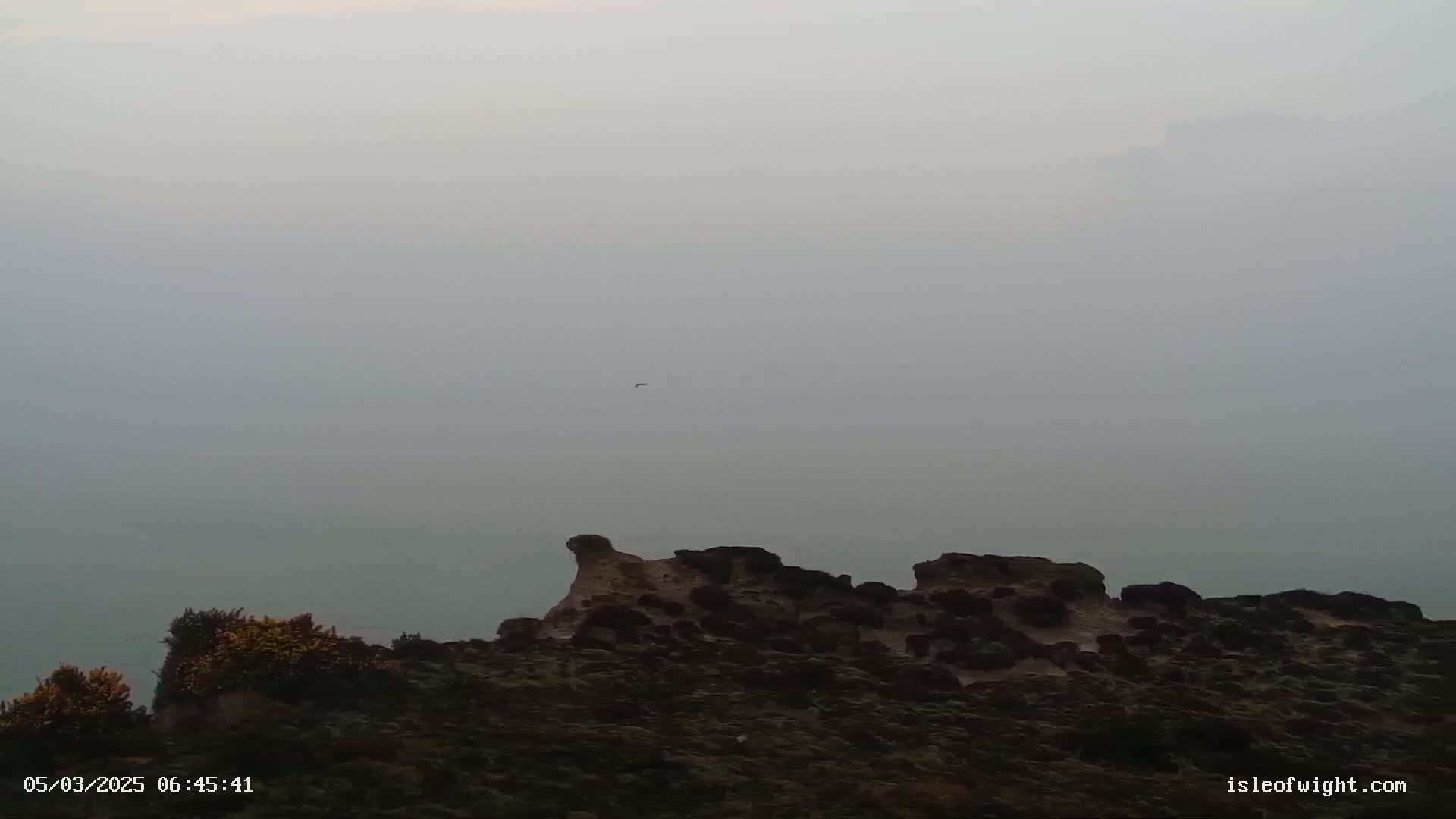 A rocky outcrop is visible in the foreground, partially obscured by fog, with a distant body of water extending to a hazy horizon.