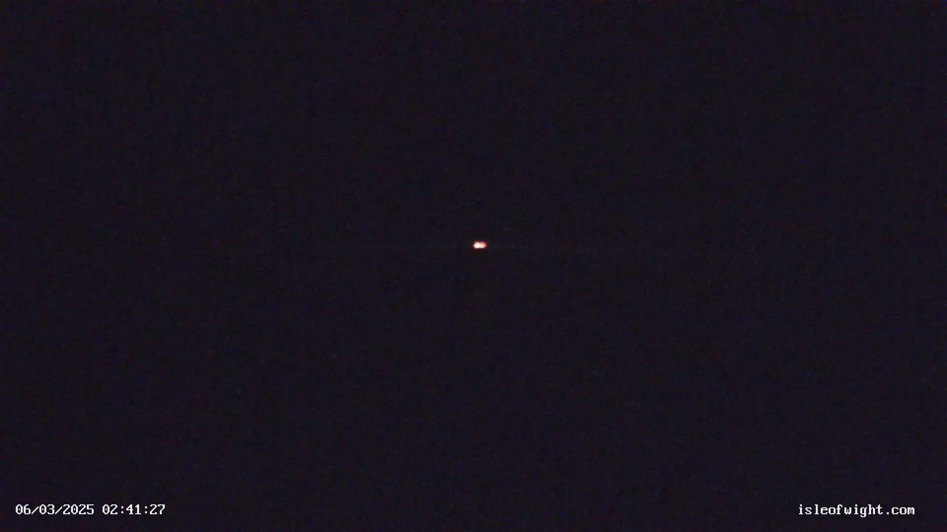 A small, faint, reddish light is visible in the center of a dark, nighttime sky.