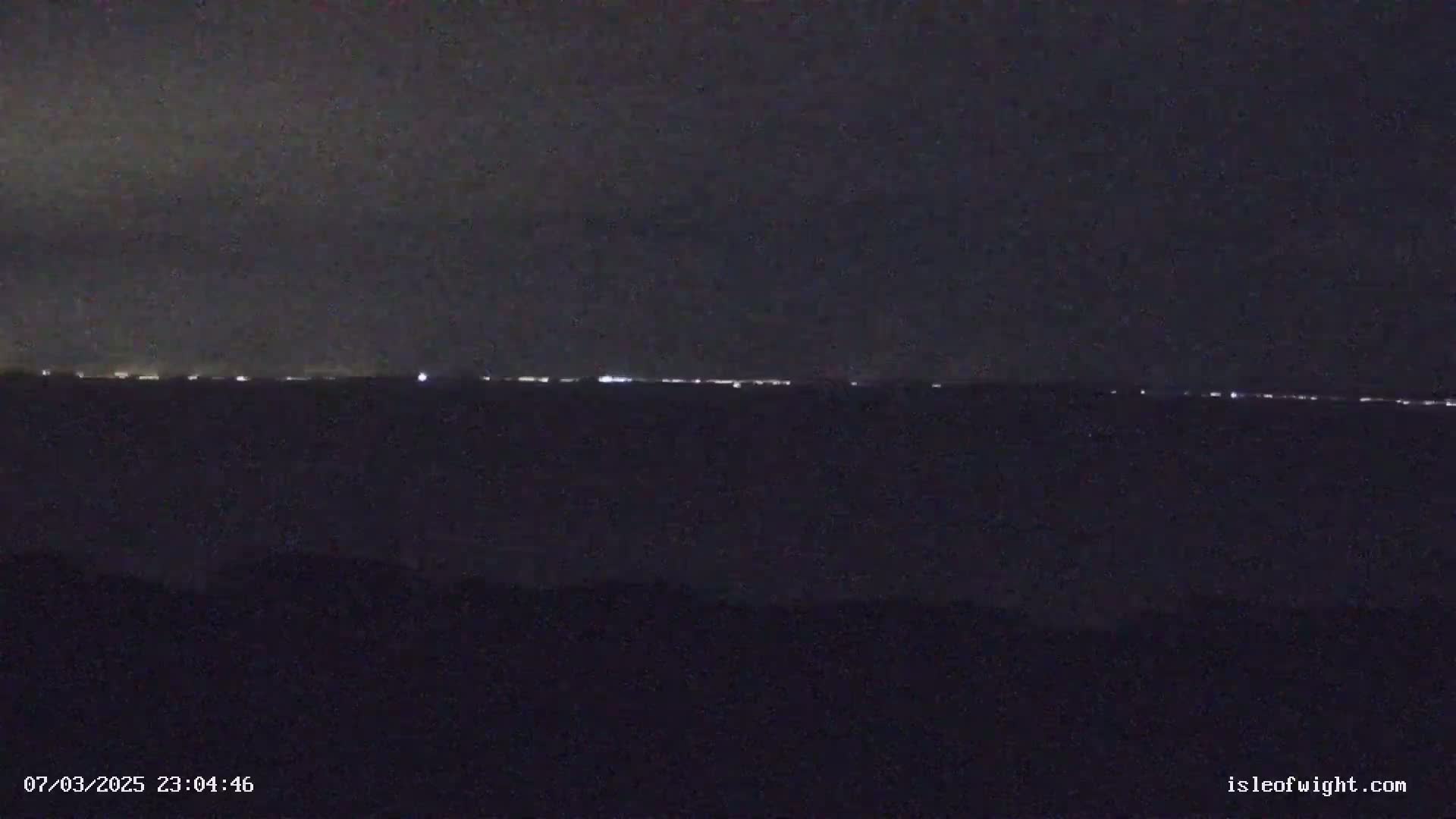 A dark, nighttime scene shows a faint line of distant lights on the horizon.