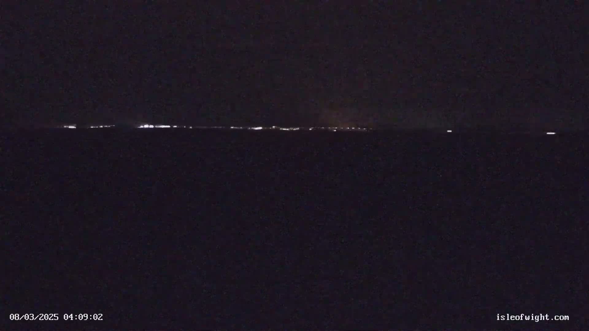 A nighttime long shot shows a distant line of lights on the horizon under a dark sky.