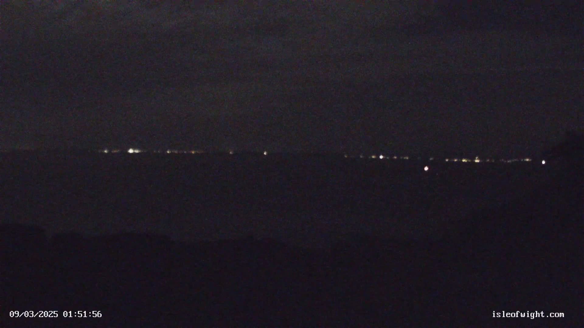 A dark, nighttime view shows a distant line of faint lights on the horizon.