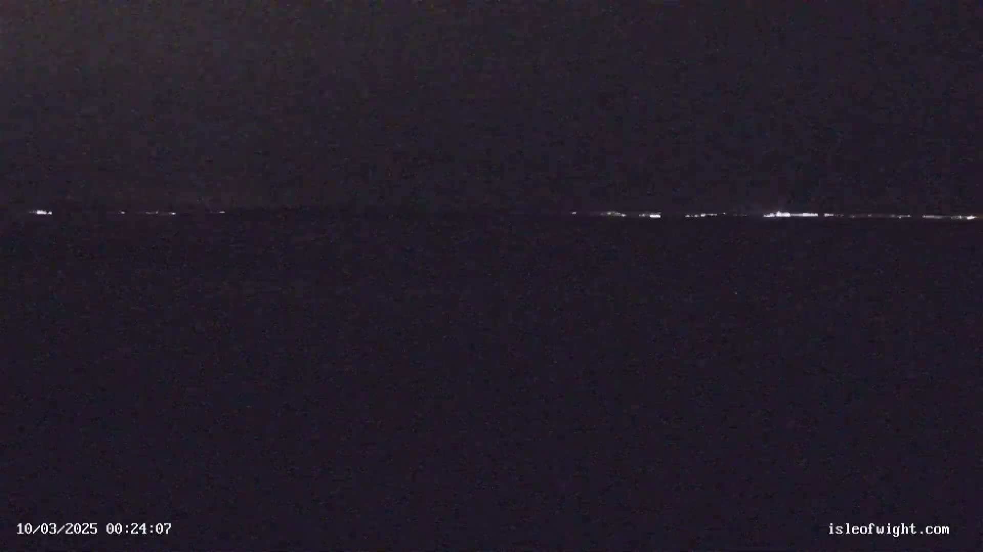 A nighttime, low-light image shows a faint line of distant lights on the horizon.