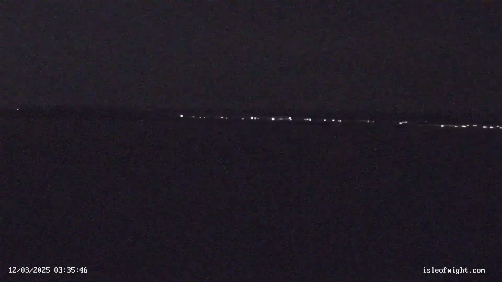 A dark, nighttime scene shows a line of faint lights on the horizon.