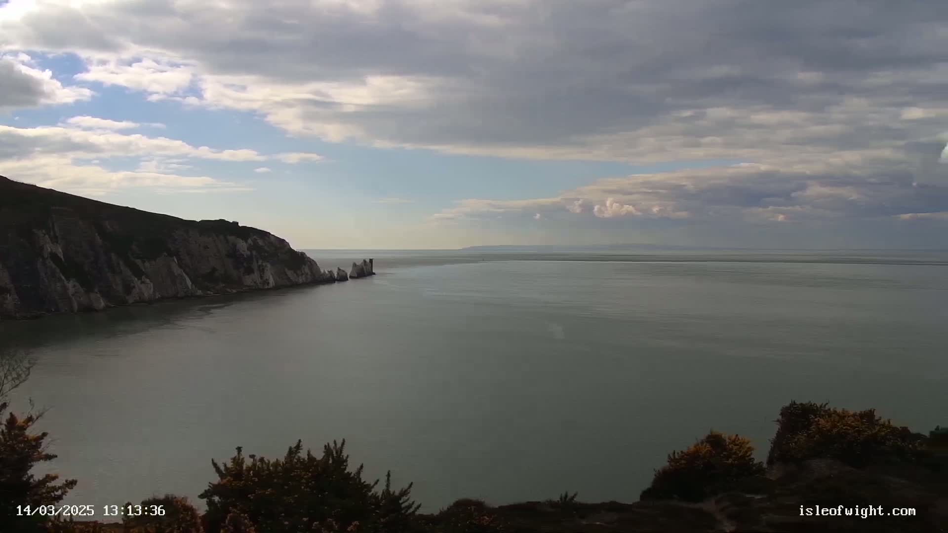 A coastal scene shows a body of calm water under a partly cloudy sky, with white cliffs and rock formations visible on one side.