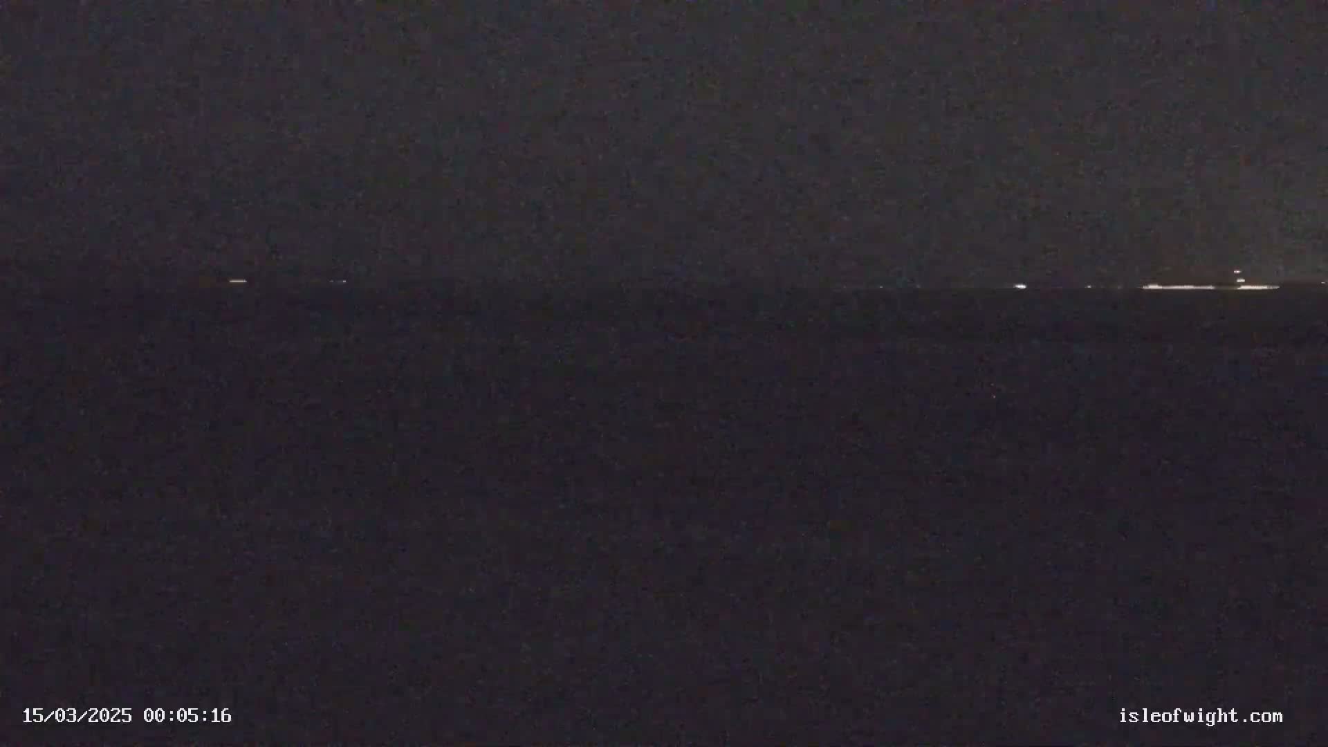 A dark nighttime view shows a distant horizon line with faint lights possibly from ships or shore lights.
