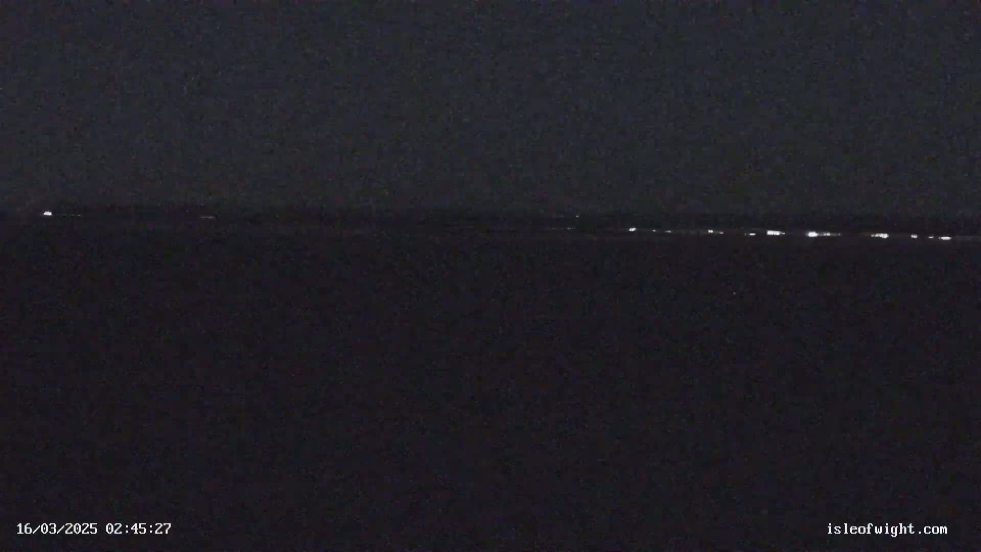 A dark, nighttime scene shows a distant line of lights on the horizon.