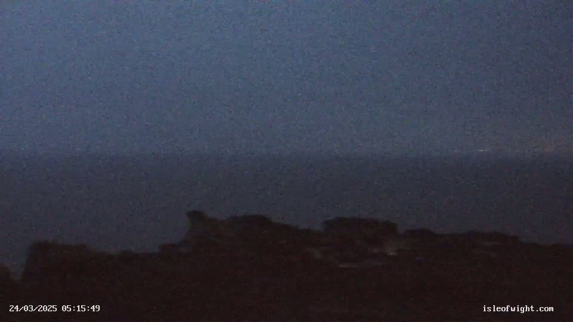 A dark, possibly overcast, sky looms over a dark, indistinct shoreline and a body of dark water.