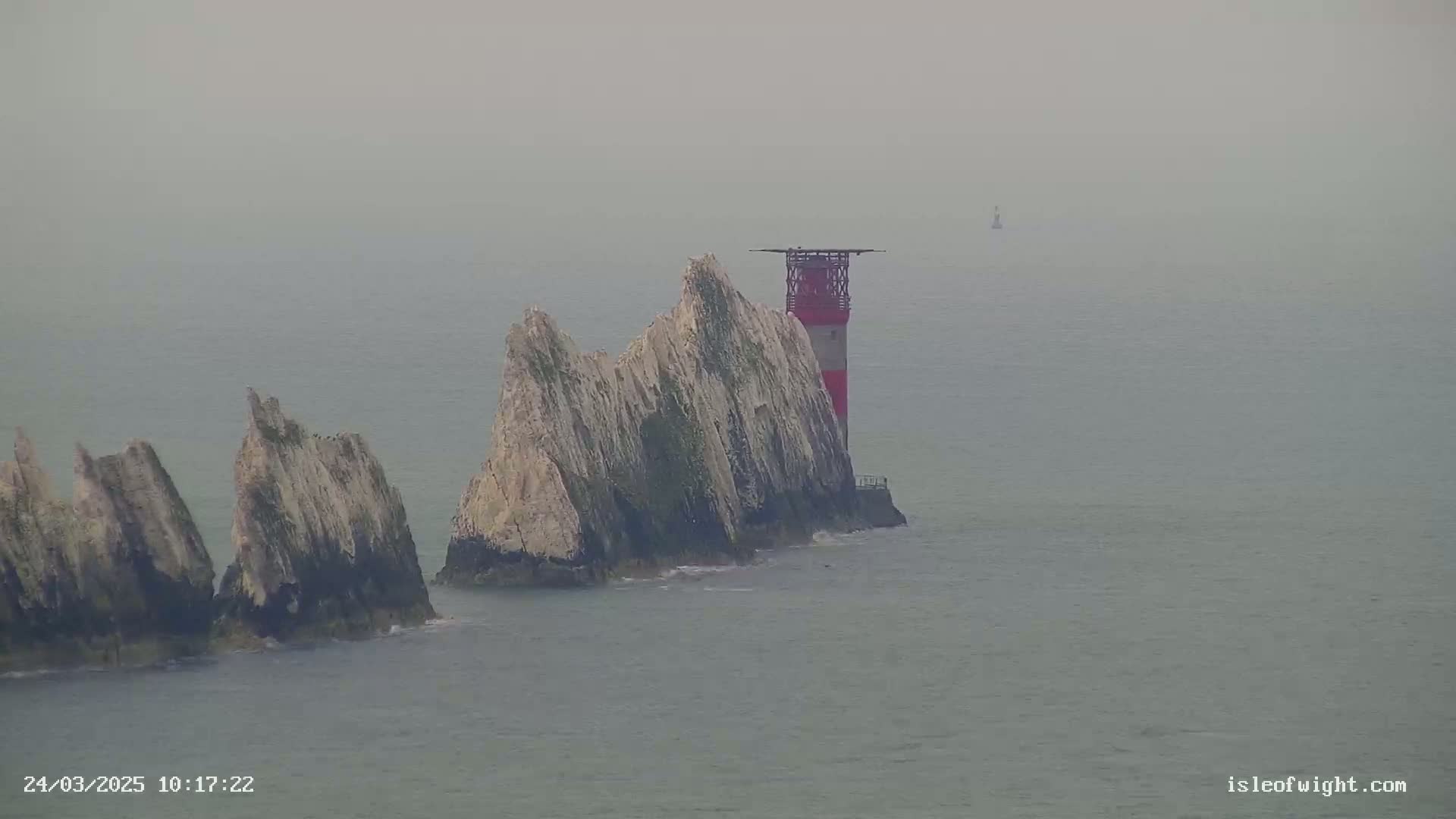 A red and white lighthouse stands atop a cluster of rocky islands in foggy conditions.