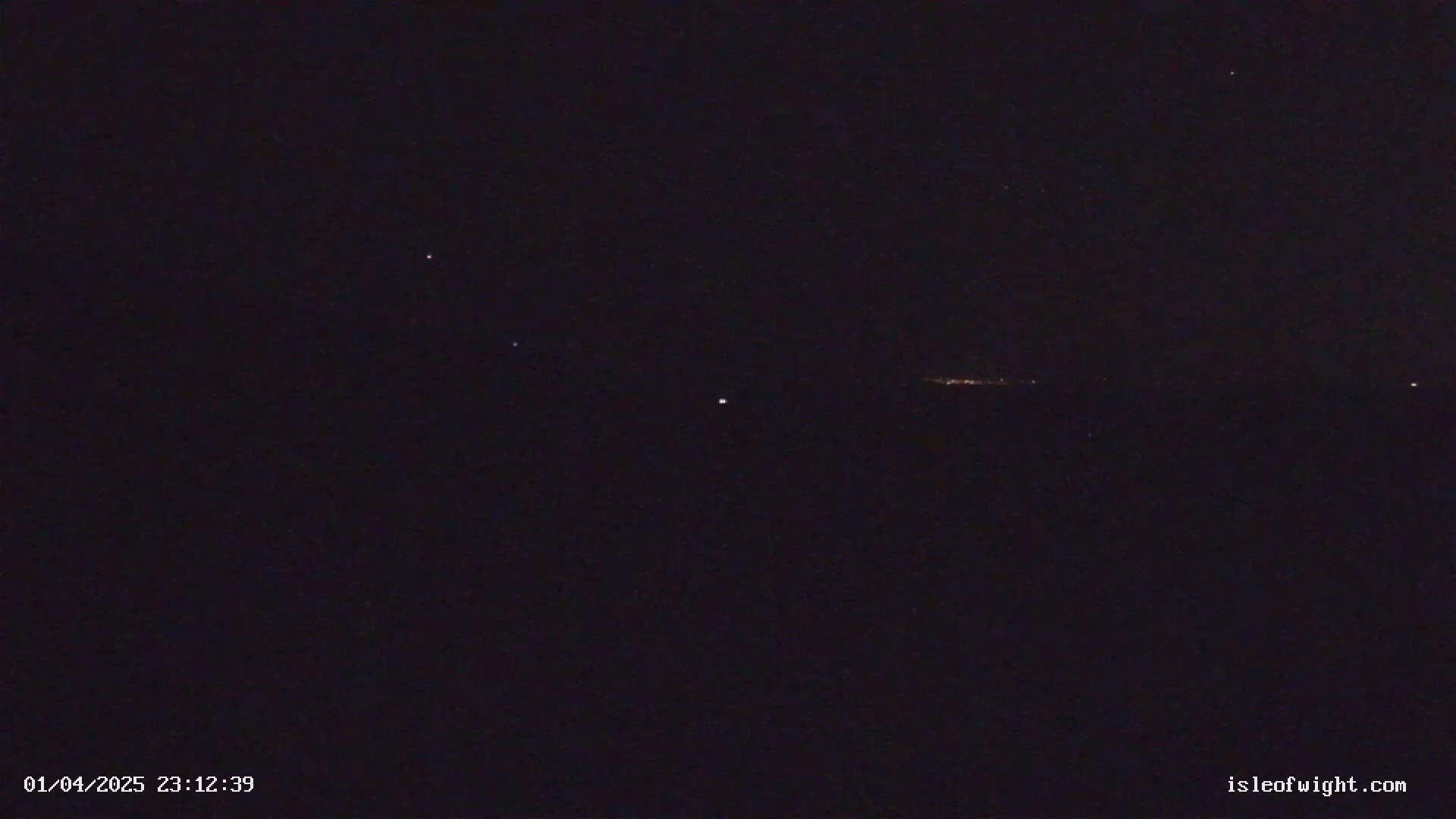 A nighttime, dark sky shows a few stars and a distant line of faint lights on the horizon.