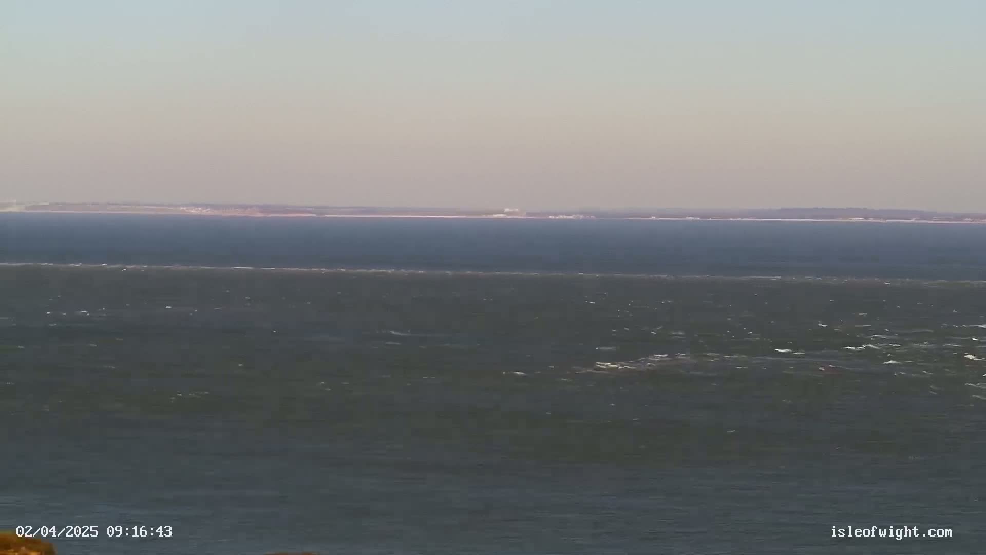 A wide shot of a choppy sea with a distant landmass visible on the horizon under a clear sky.