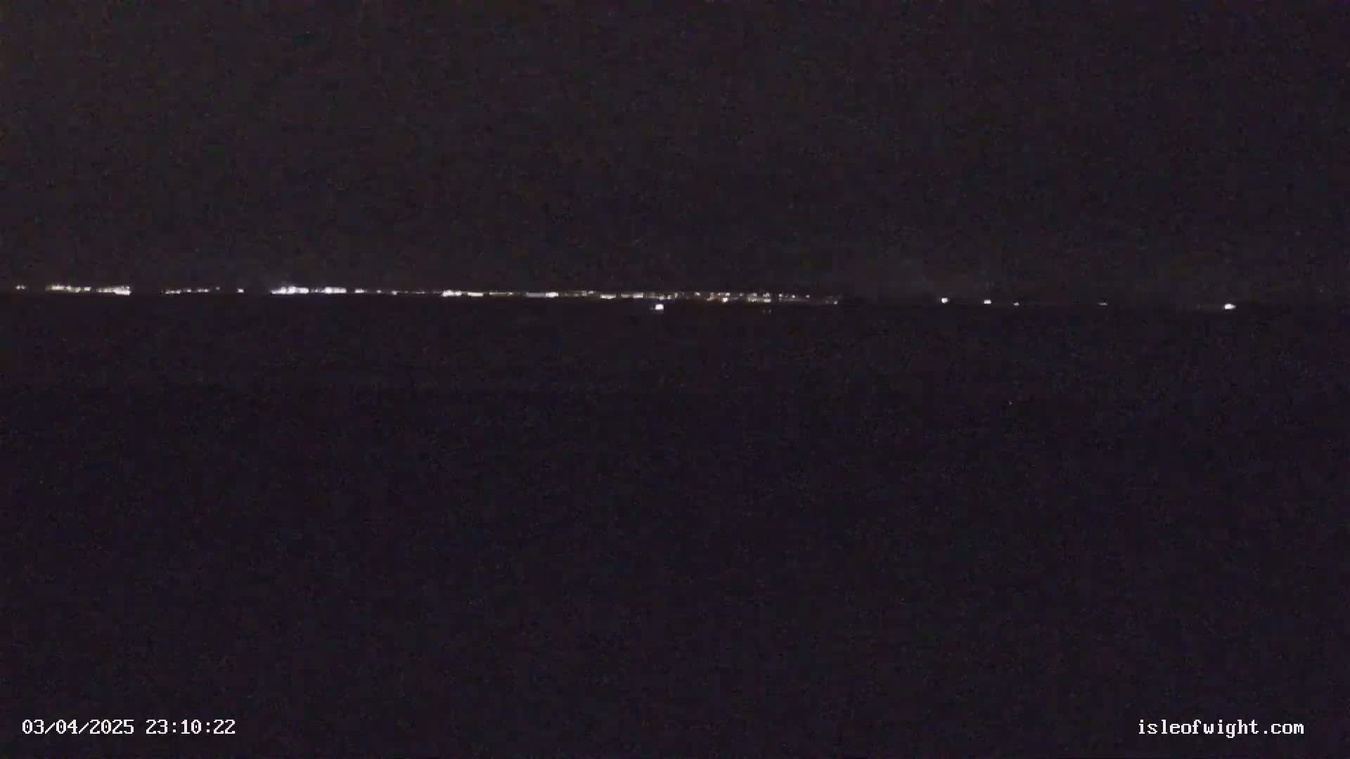 A dark, nighttime landscape shows a faint line of distant lights on the horizon.