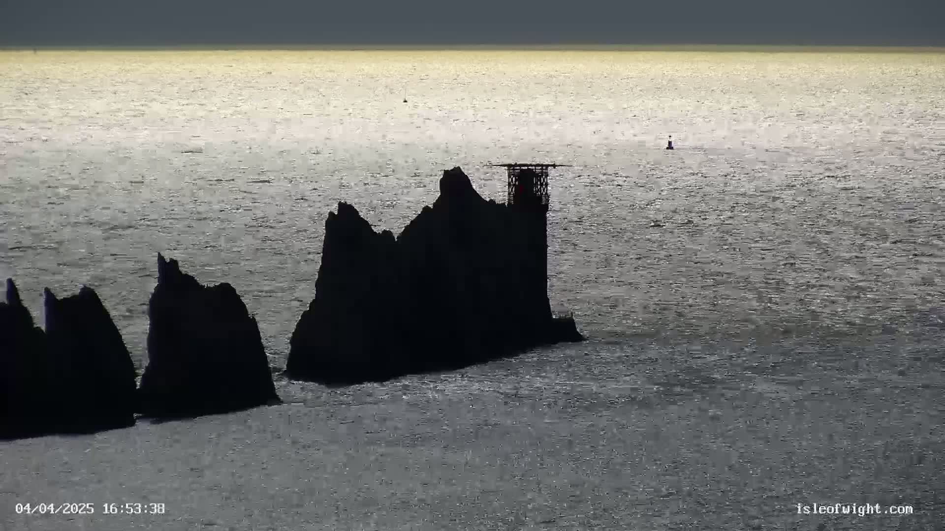 Silhouetted rocky islands with a small structure on the largest one are visible in a calm, gray sea under a dark sky.