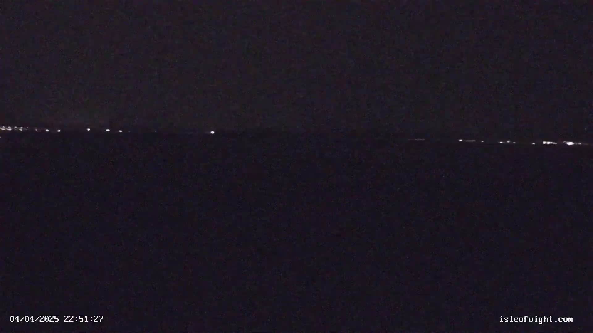 A dark, nighttime scene shows a distant line of faint lights on the horizon.