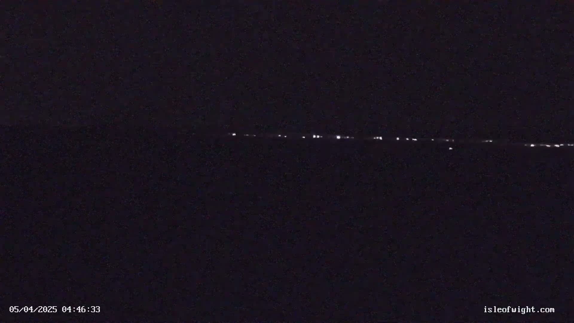 A dark nighttime scene shows a distant line of faint lights on the horizon.