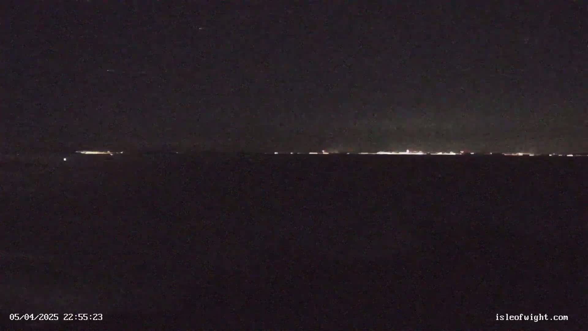 A dark, nighttime landscape shows a distant line of faint lights on the horizon under a clear, starless sky.
