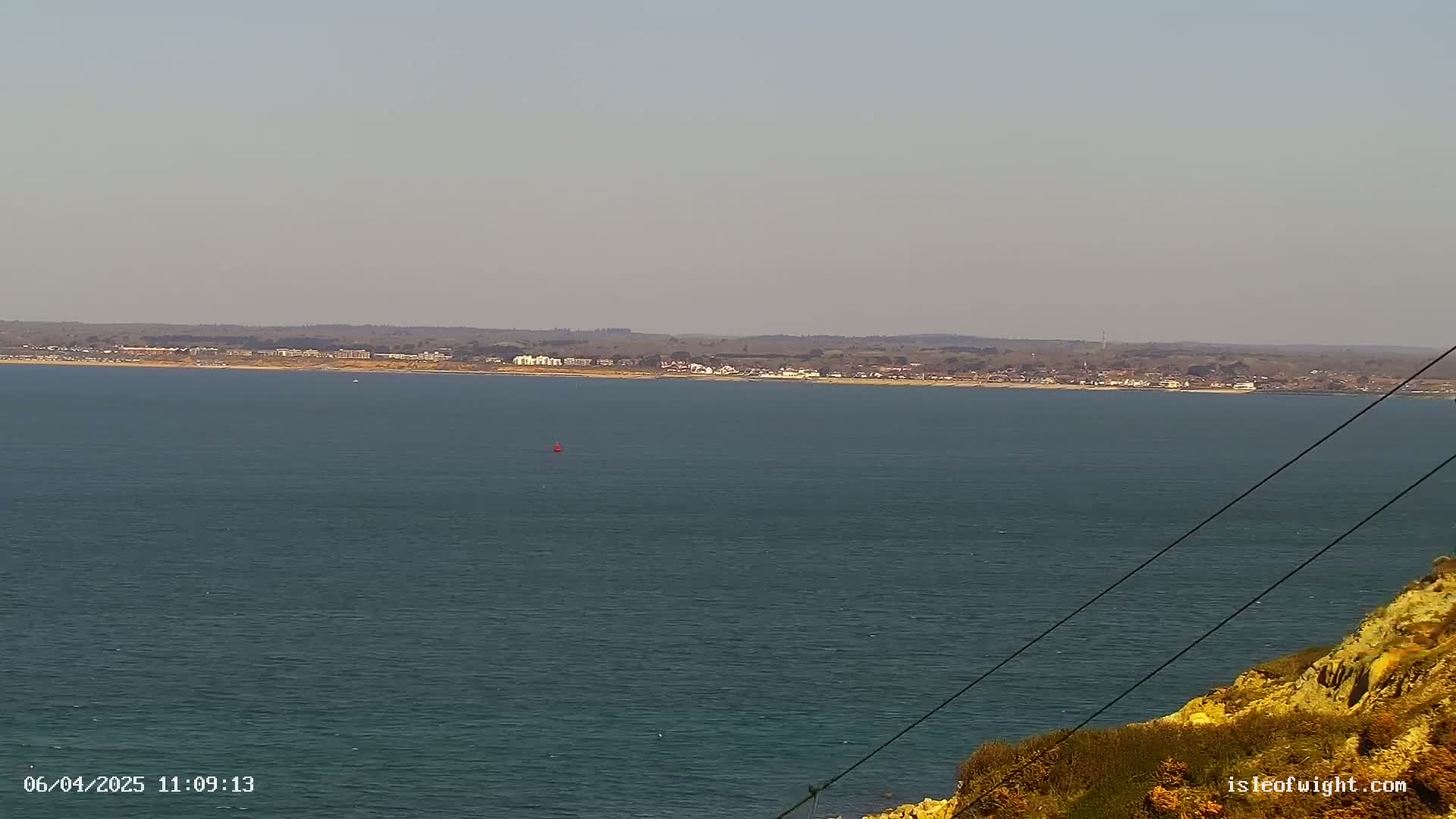 A calm body of water stretches to a distant shoreline featuring buildings and low-lying land under a clear sky.