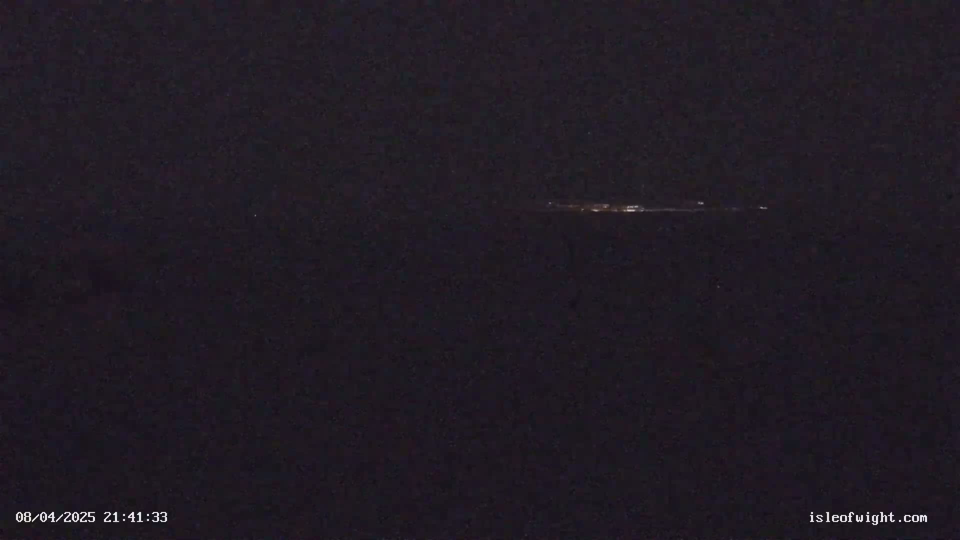 A dark, nighttime scene shows a faint line of lights on the horizon.