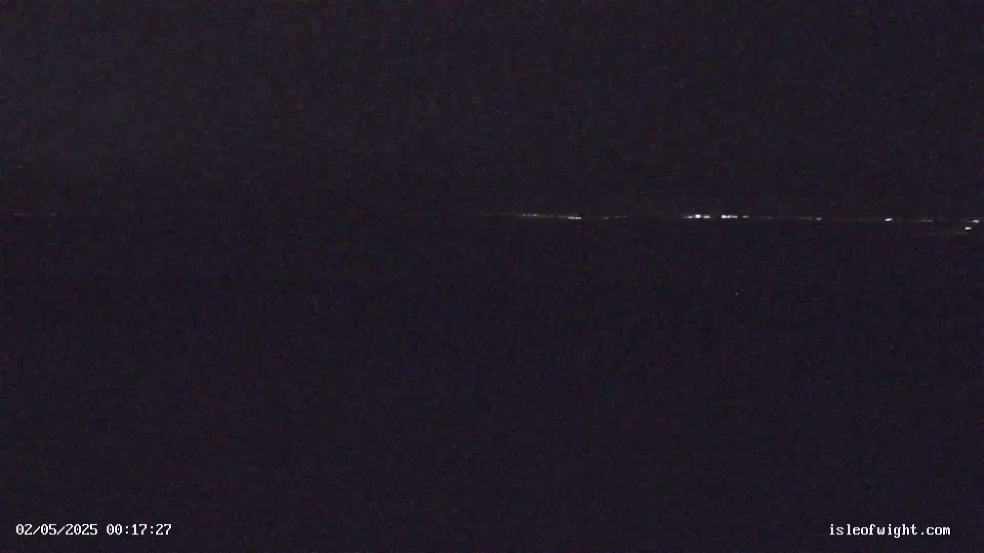 A dark, nighttime scene shows a distant line of faint lights on the horizon.