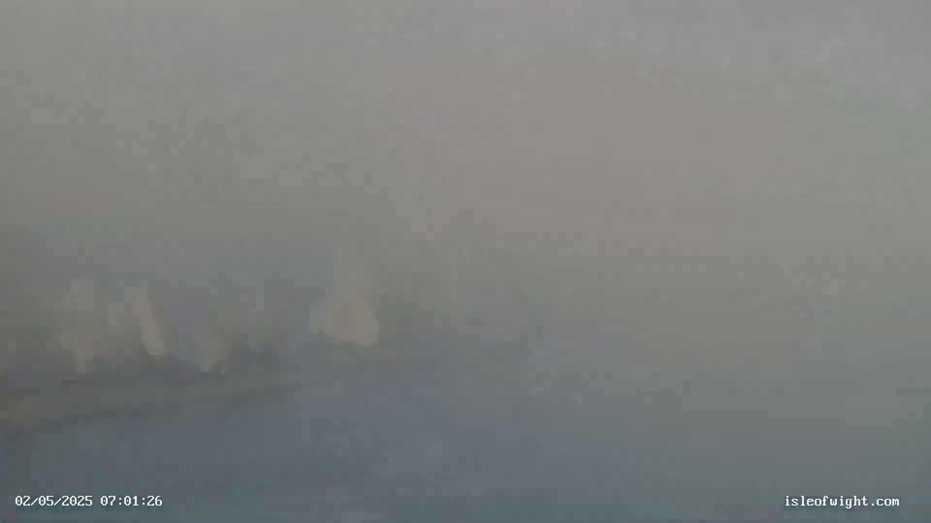A hazy, foggy scene shows indistinct shapes that appear to be buildings or structures in the distance.