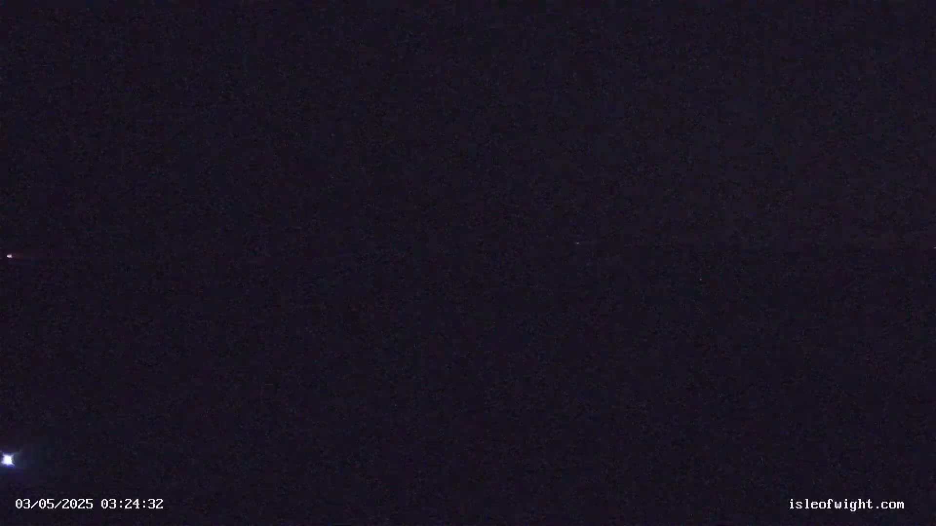 A dark, nighttime outdoor scene shows a few faint lights in the distance against a mostly clear, dark sky.