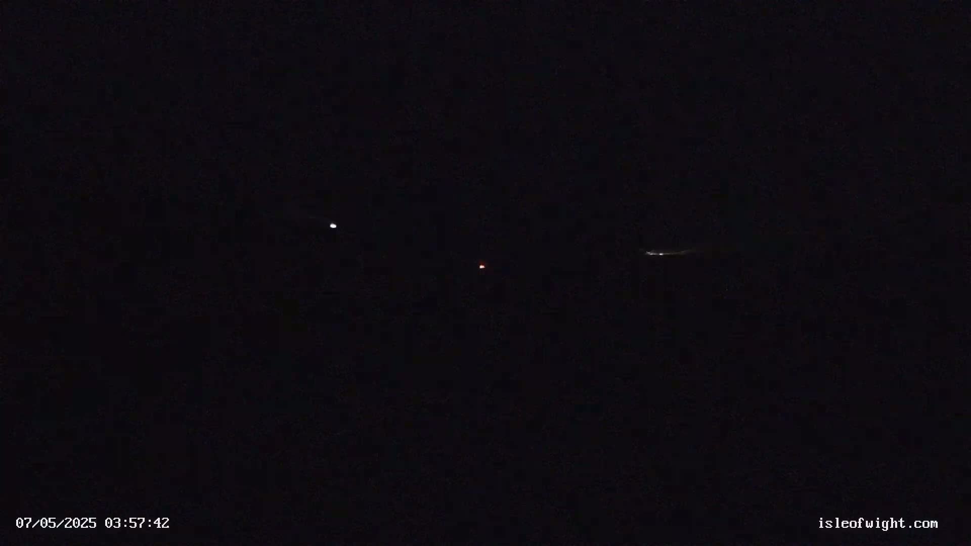 A dark night sky shows two bright lights and one faint red light, along with a faint streak of light.