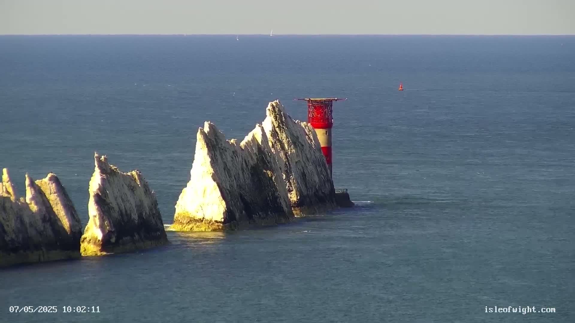 A red and white lighthouse stands atop a group of tall, white, jagged rocks in a calm sea.