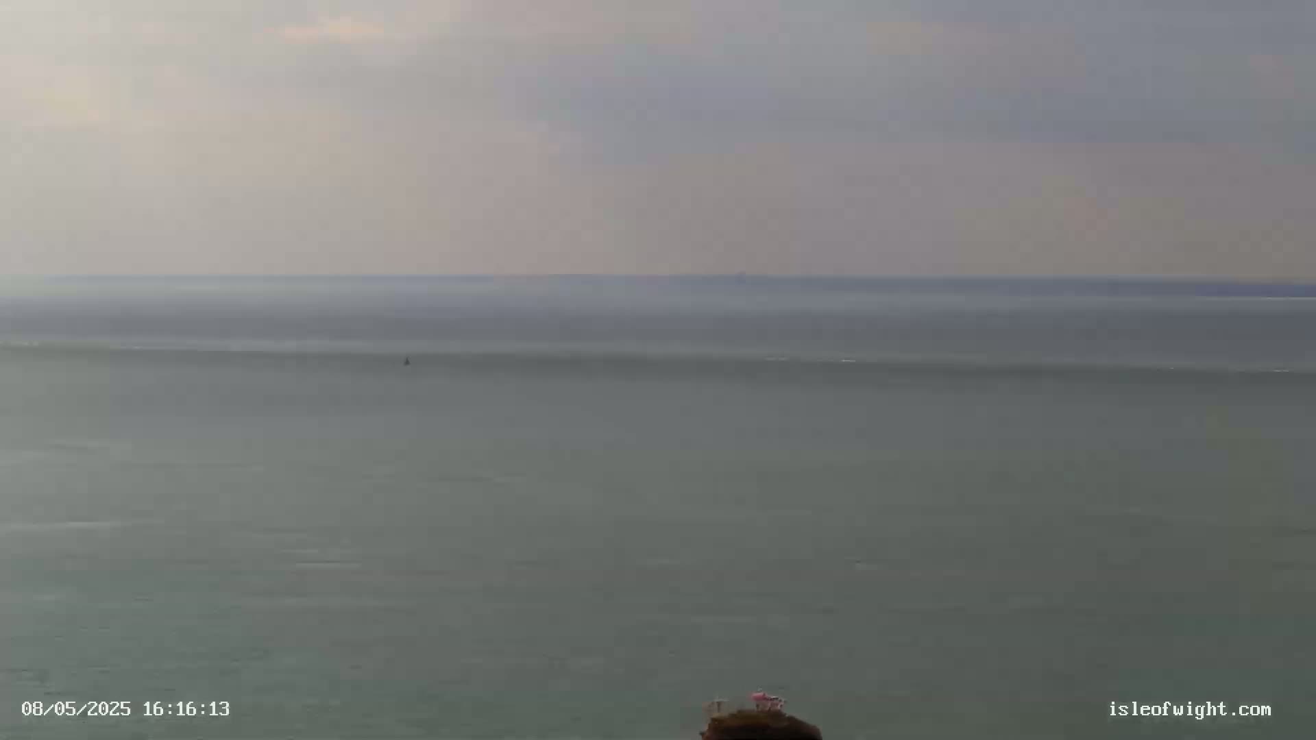 A calm, overcast day shows a wide expanse of gray-green sea extending to a hazy horizon.