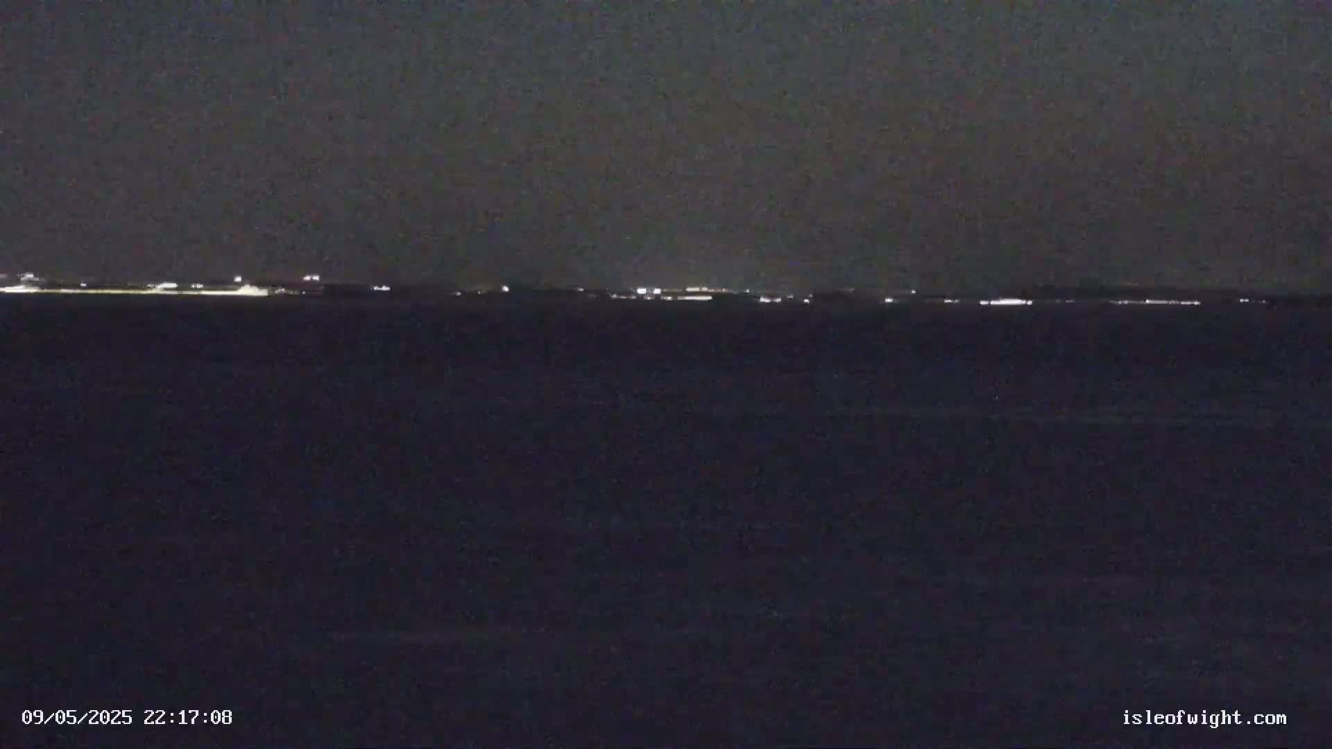 A dark body of water at night shows a distant, faintly lit shoreline under a dark sky.