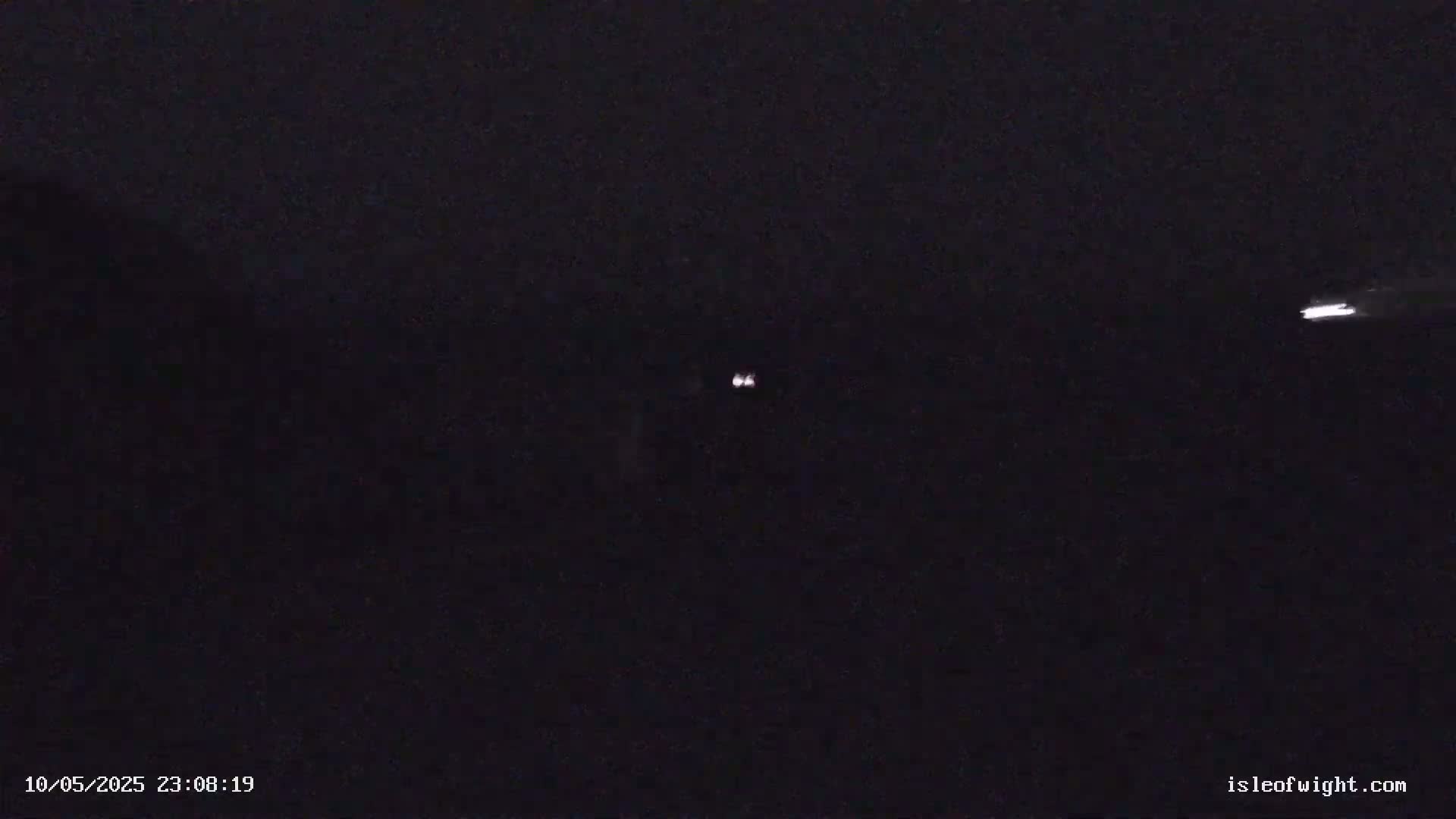 A dark nighttime scene shows two small, distant lights and a faint horizontal streak of light in the sky.
