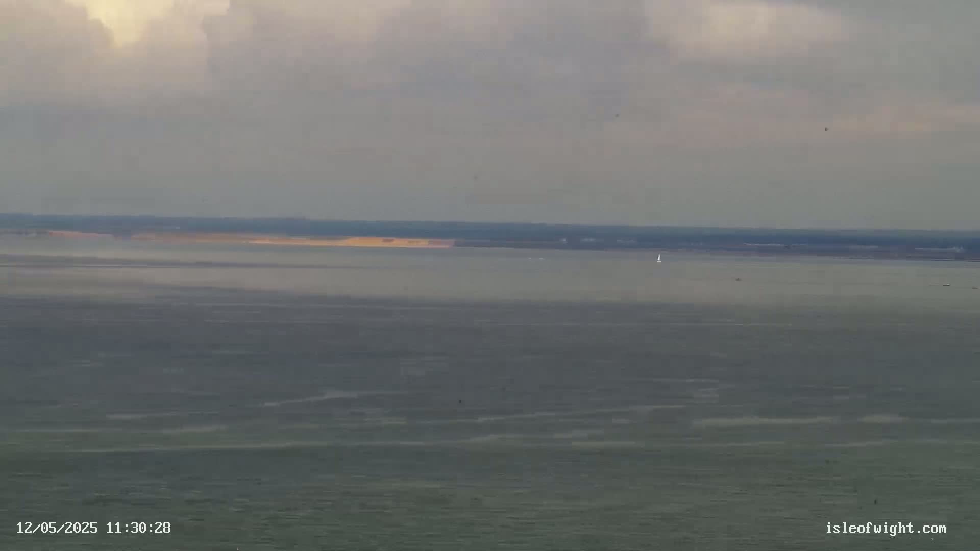 A calm, overcast day shows a wide expanse of gray water with a distant shoreline and a few small boats.