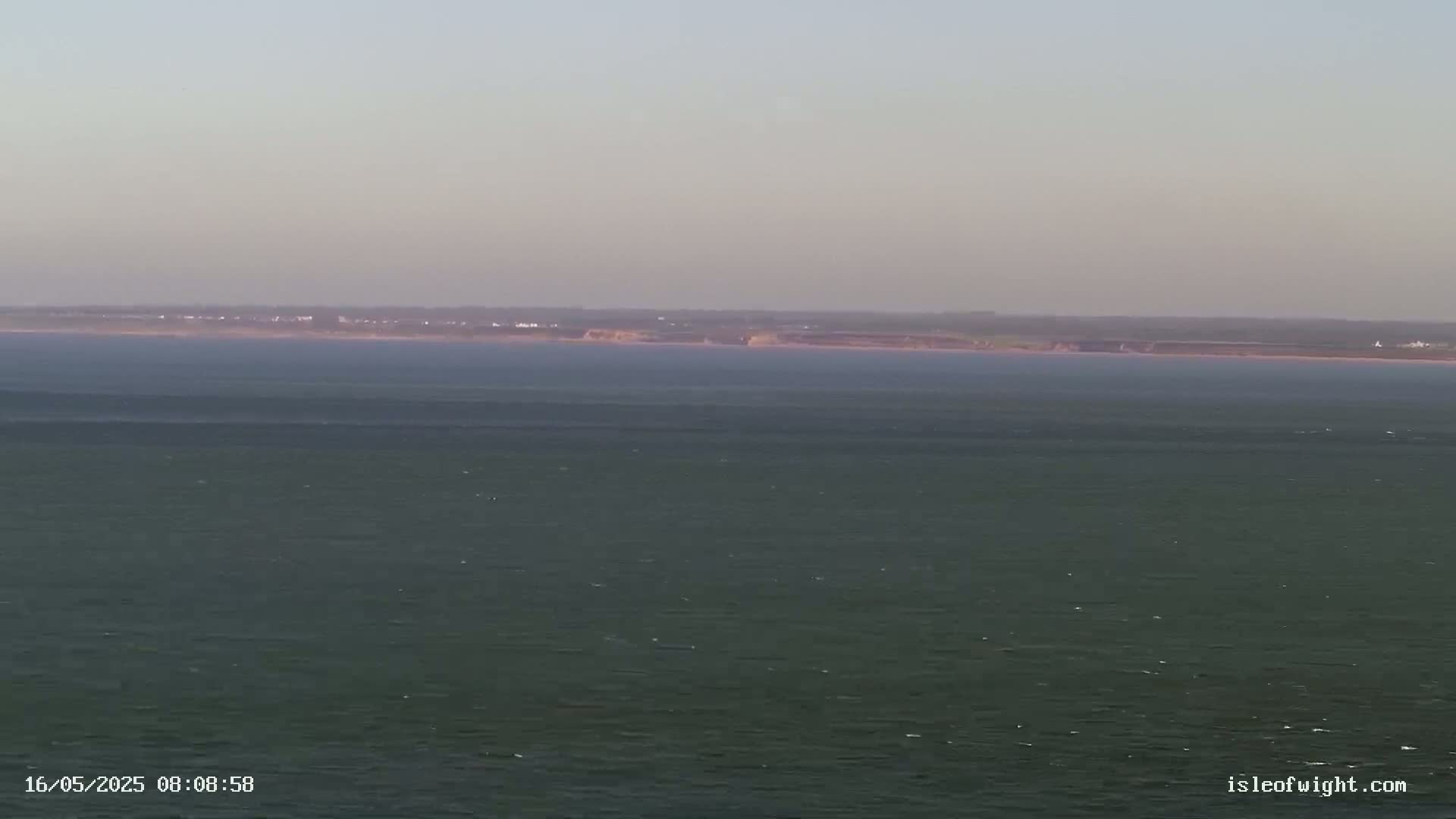 A calm, expansive body of water stretches to a distant shoreline under a hazy sky.