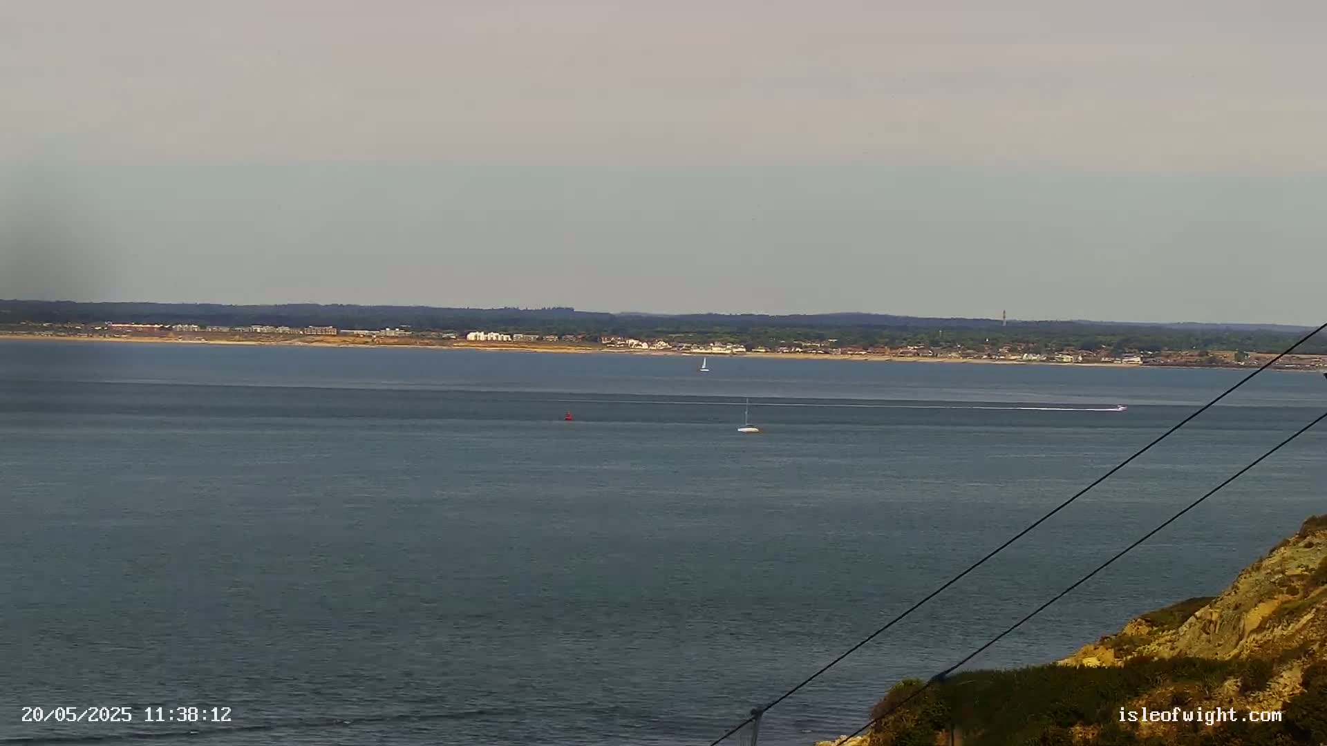 A calm, overcast day shows a wide expanse of gray-blue water with a few small boats and a distant shoreline.