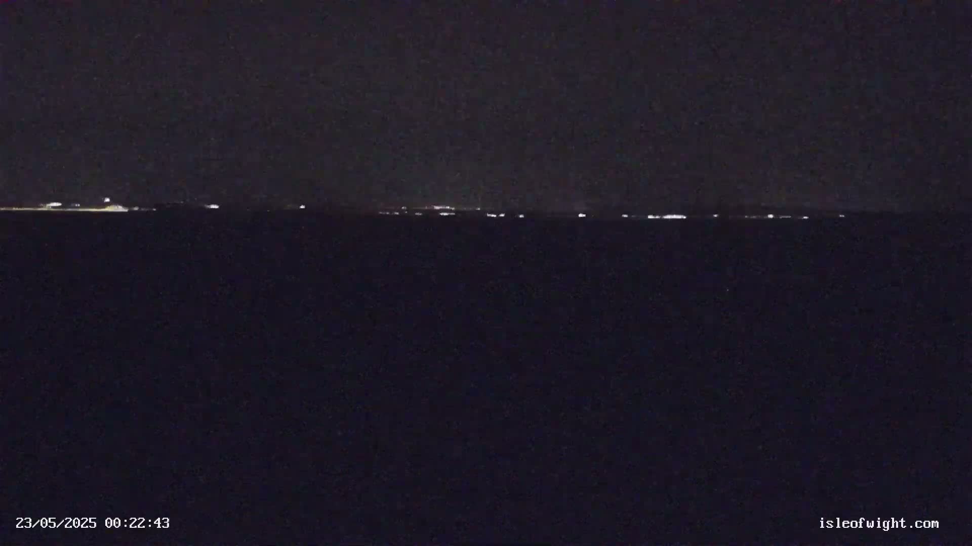 A dark, nighttime scene shows a distant line of faint lights on the horizon.