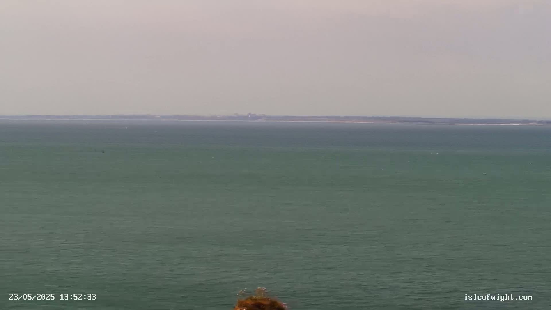 A calm, gray-skied day is shown over a large body of dark-green water, with a distant landmass visible on the horizon.