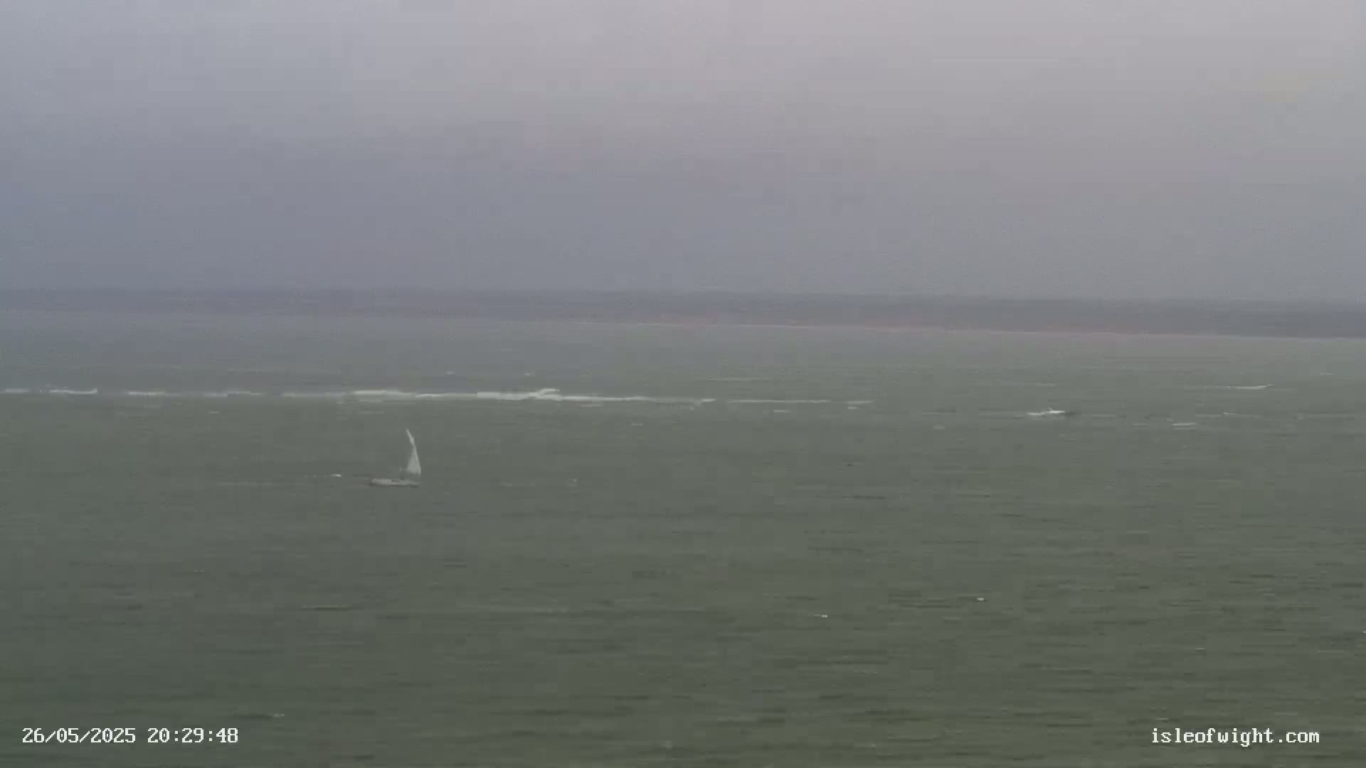 A sailboat is visible on a choppy, gray sea under an overcast sky.